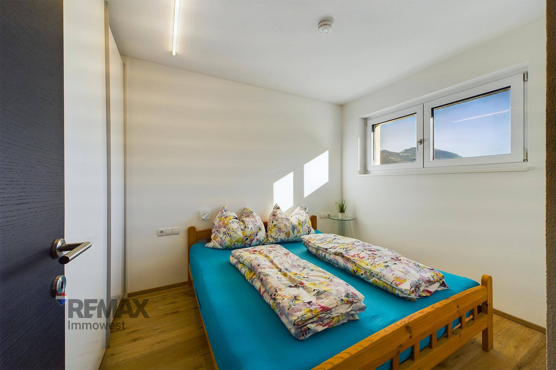 Gemütliches Schlafzimmer mit Holzbett, Holzboden und Fenster mit Bergblick.