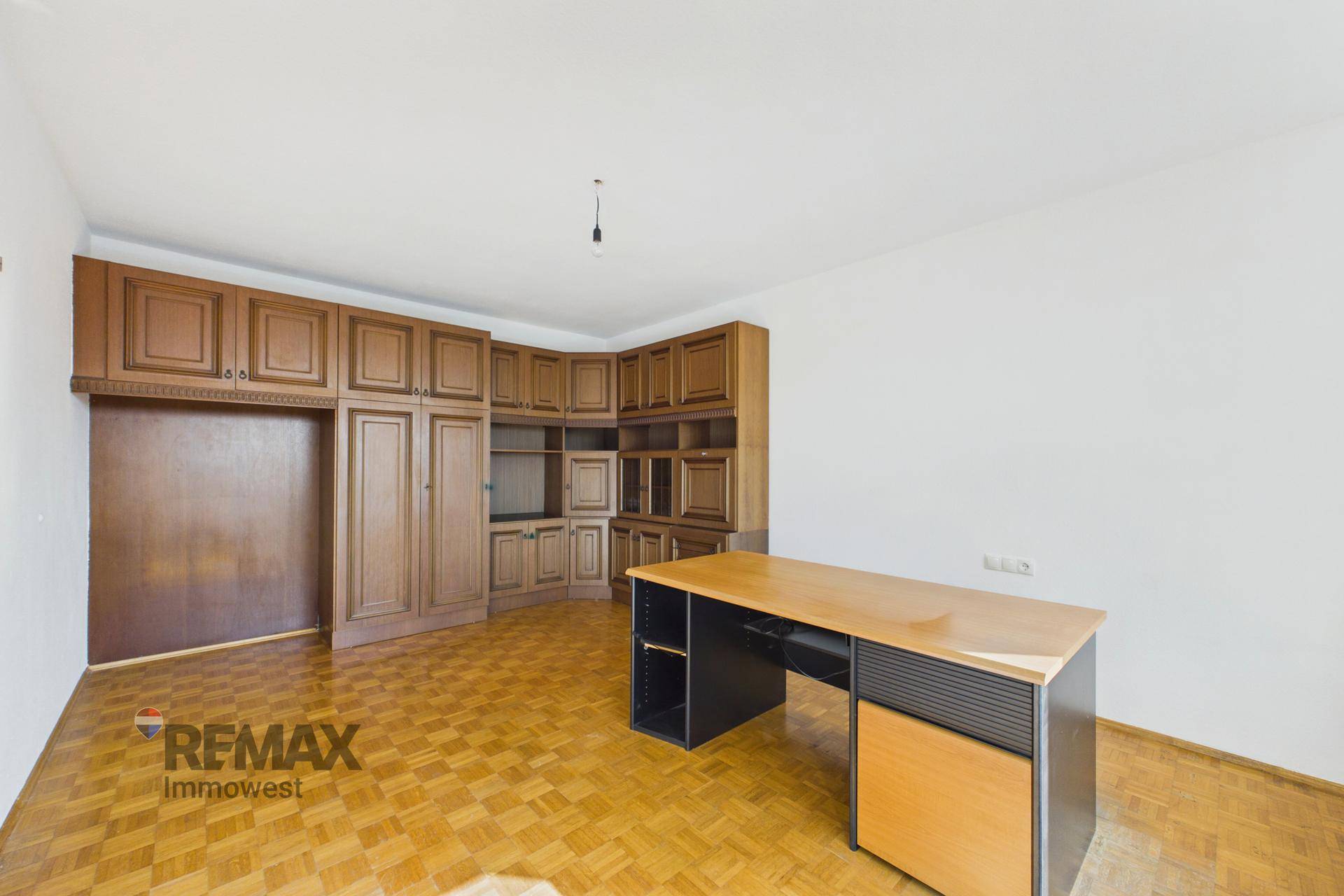 Helles Arbeitszimmer mit umfangreichen Einbauschränken aus Holz und Parkettboden.