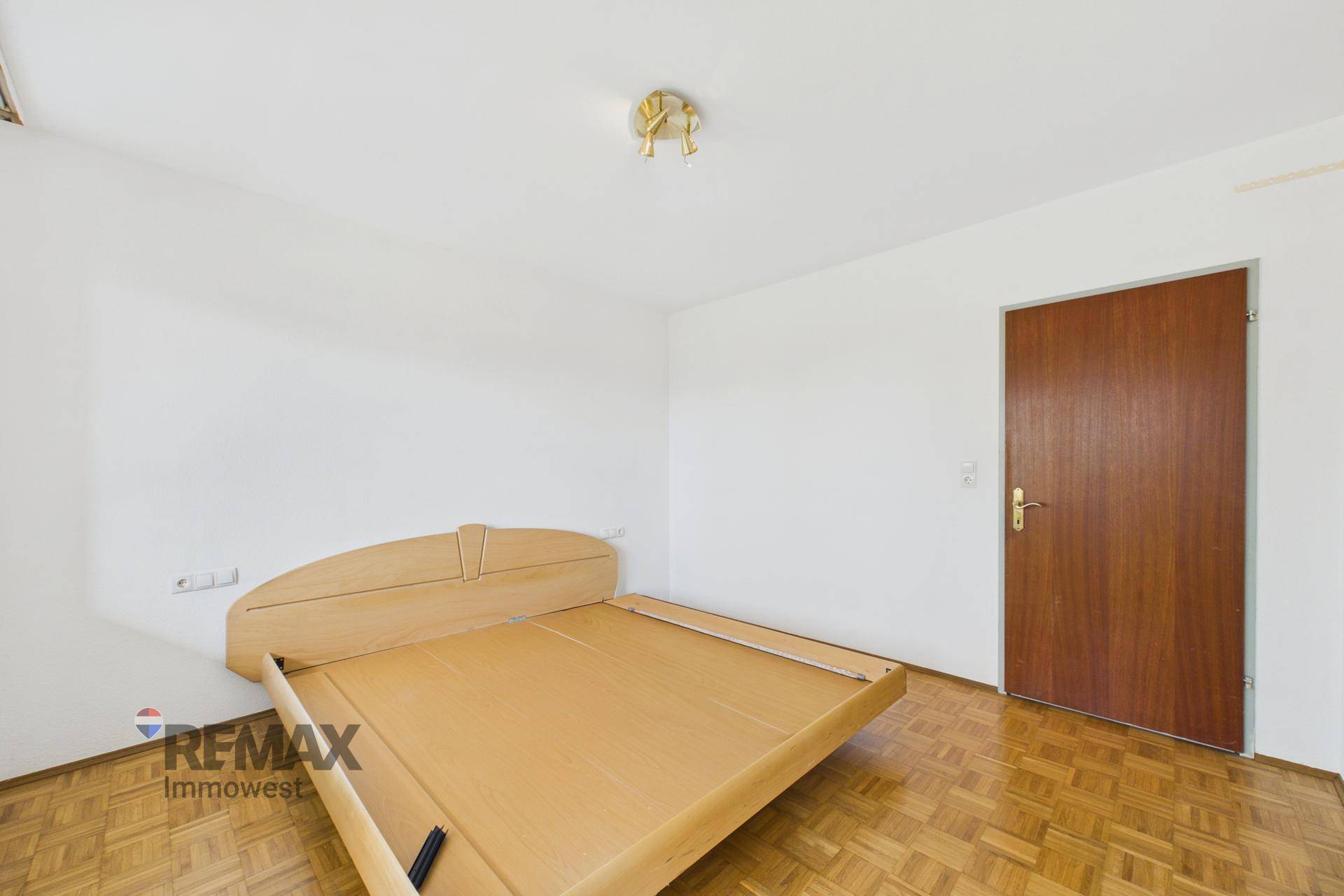 Helles Schlafzimmer mit Parkettboden und einer Holztür, bereit zur individuellen Gestaltung.