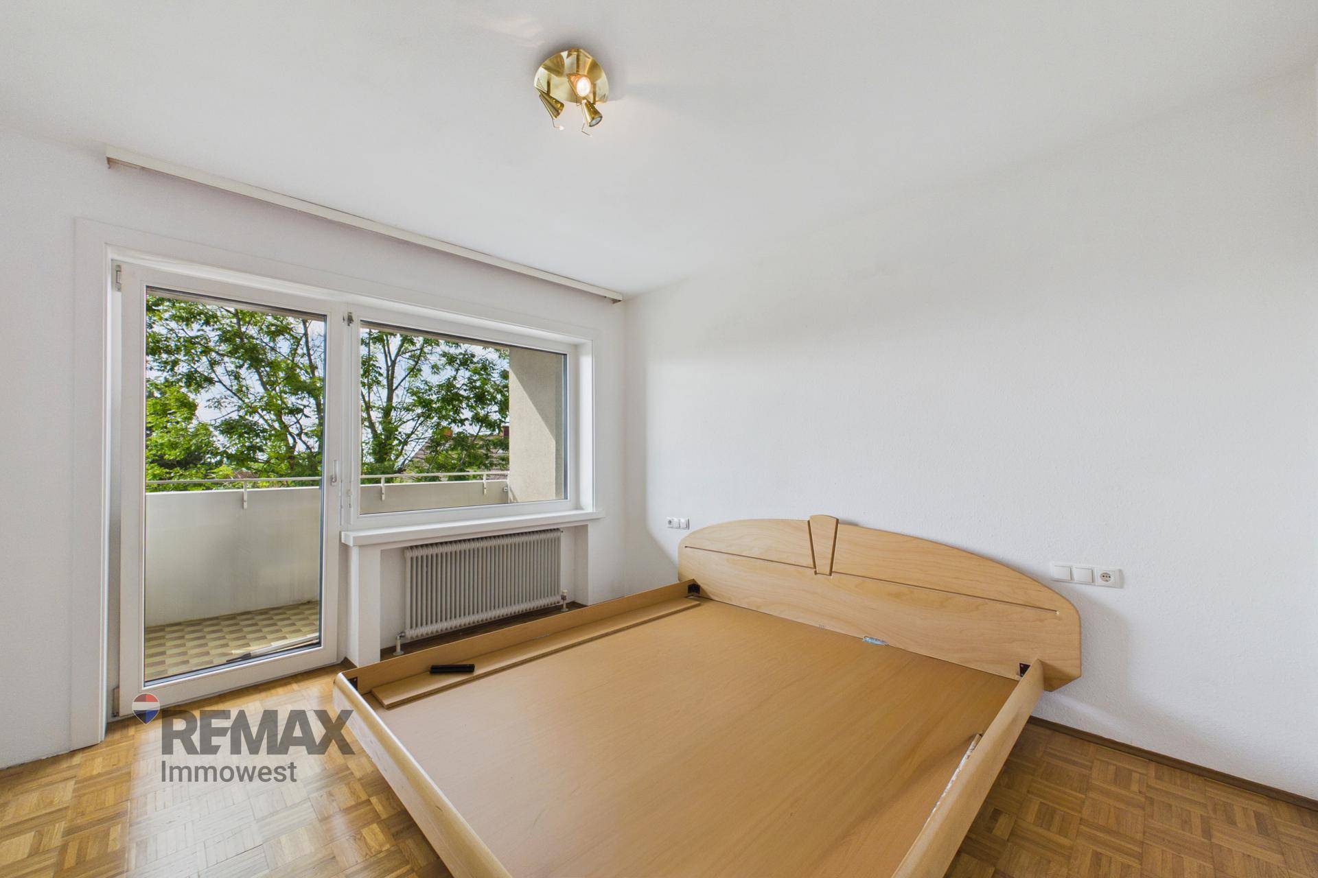 Schlafzimmer mit Holzbettrahmen, Parkettboden und direktem Zugang zum sonnigen Balkon.