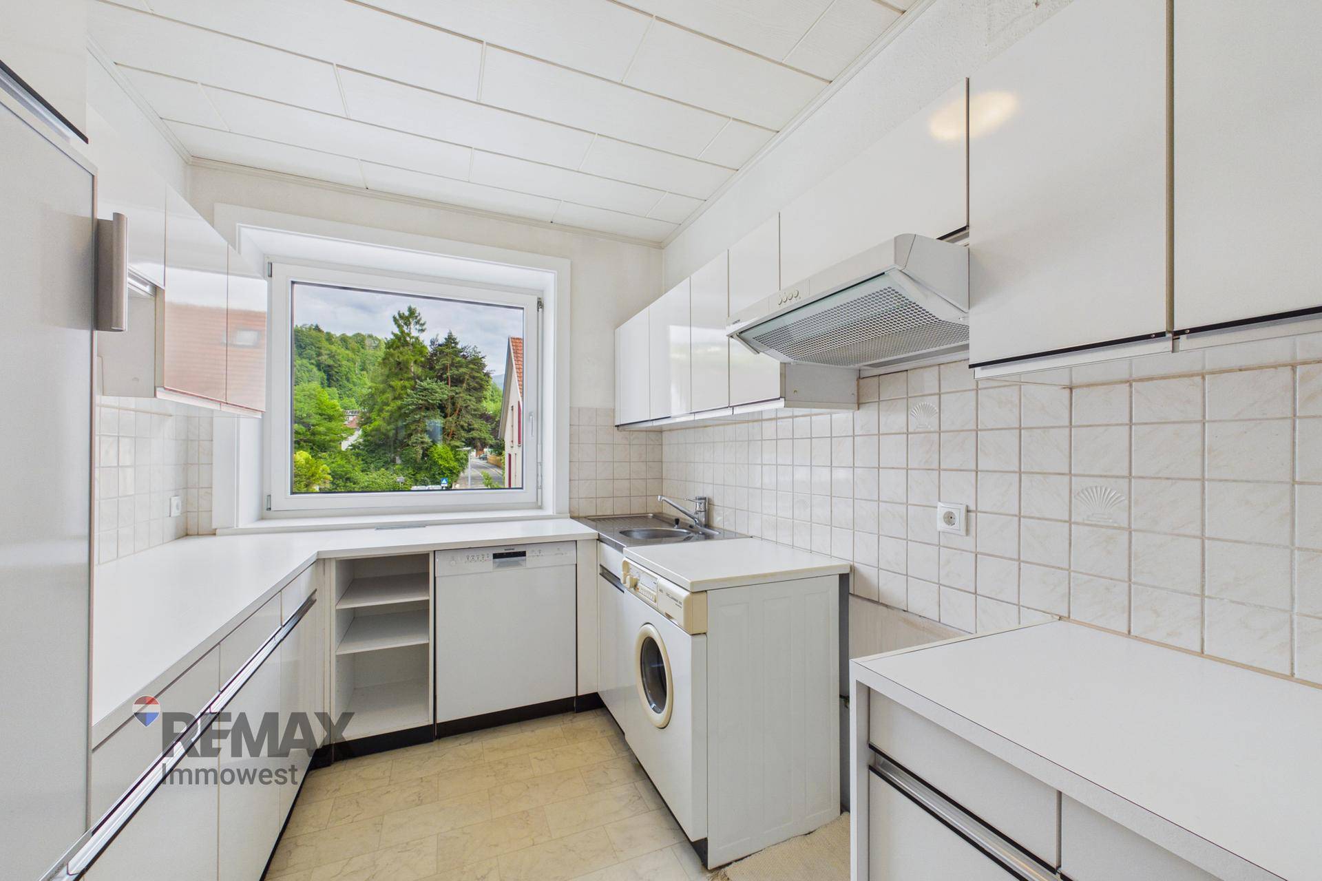 Funktionale Küche mit weißen Schränken, Fenster und integrierter Waschmaschine.