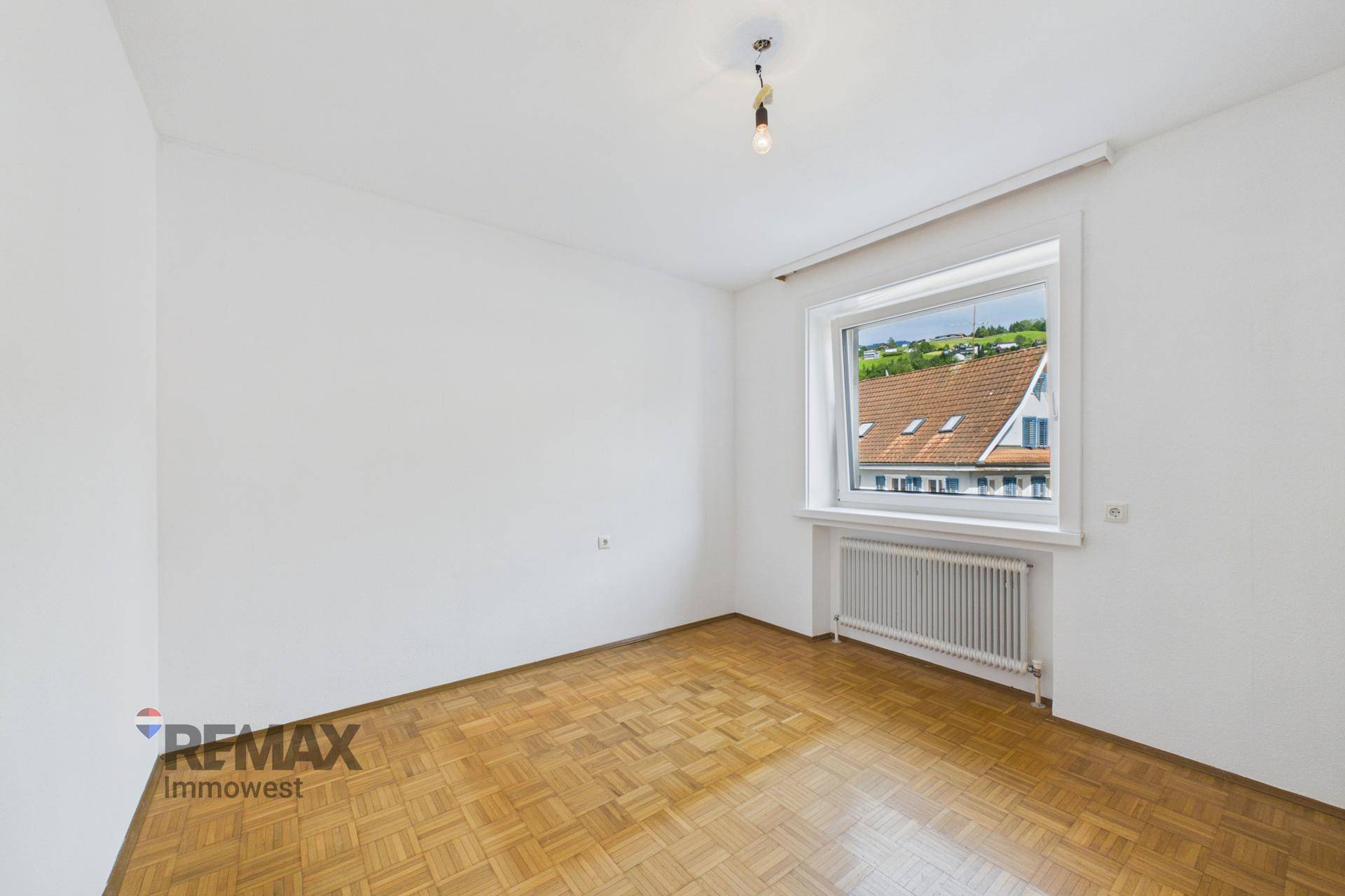Helles Zimmer mit Parkettboden und Fensterblick auf ein charmantes Nachbarhaus.