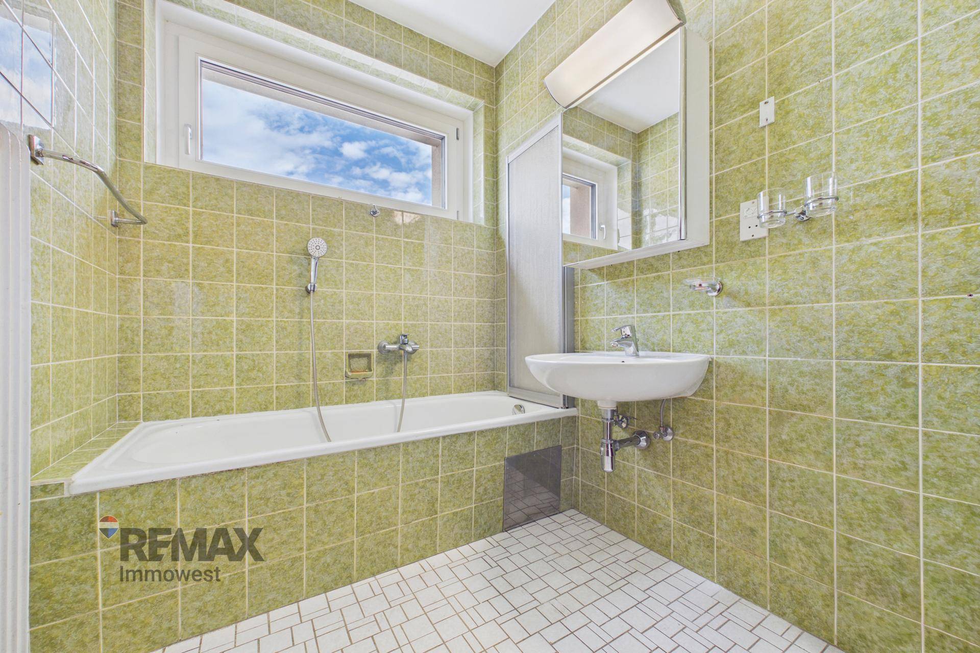 Badezimmer mit grünen Wandfliesen, Badewanne, Waschbecken und Fenster für Tageslicht.