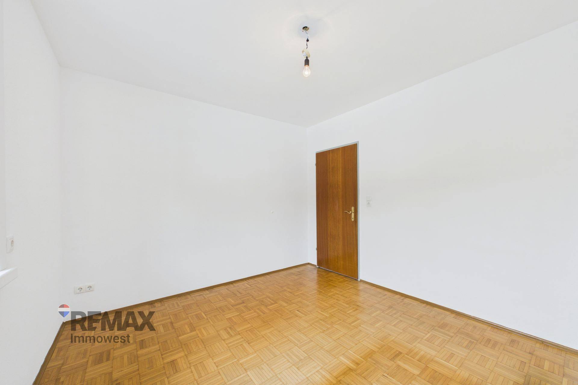 Leeres Zimmer mit Parkettboden und Holztür, bereit für individuelle Einrichtungsideen.