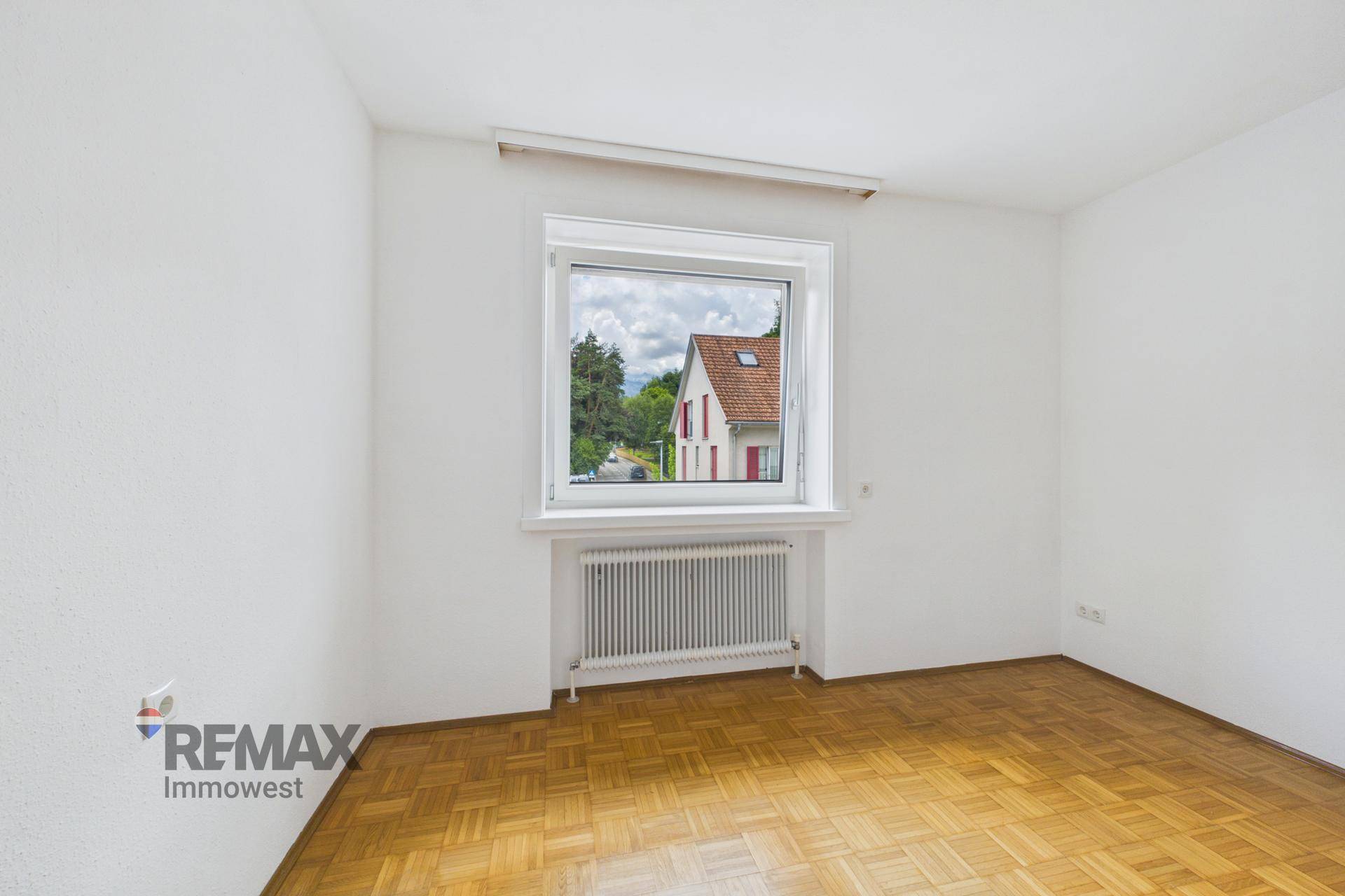 Geräumiges Zimmer mit Parkettboden und Fenster, das einen Blick auf die Umgebung bietet.