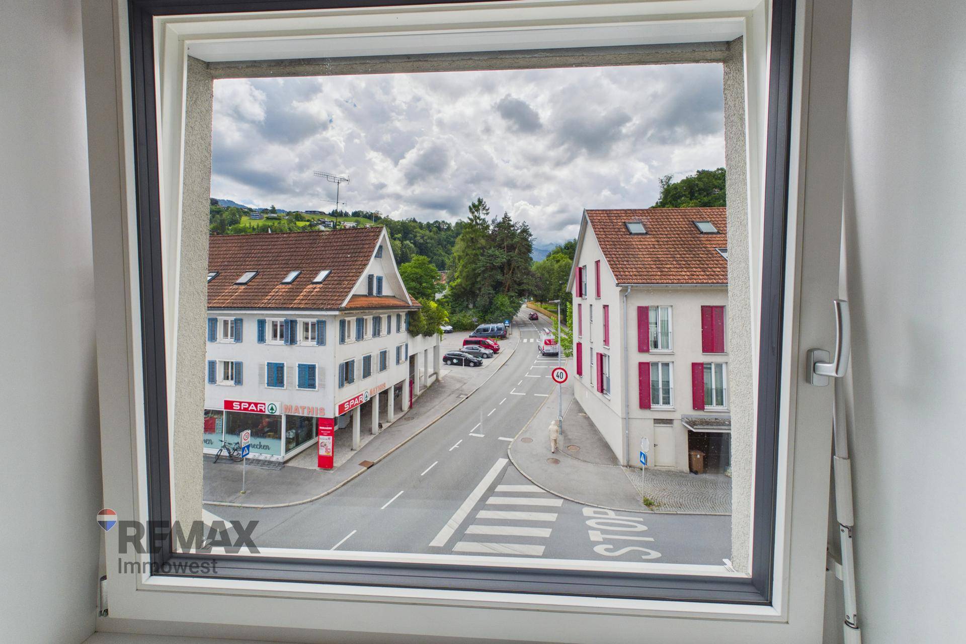 Blick aus dem Fenster auf eine belebte Straße mit Geschäften und Wohnhäusern.