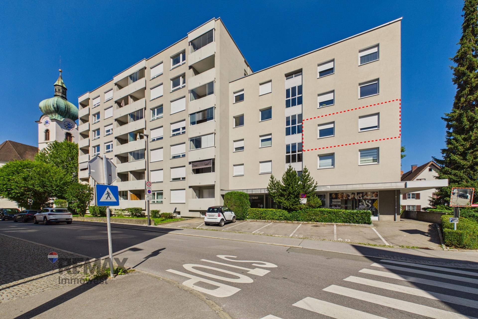 Ansicht des Mehrfamilienhauses von der Straße mit Parkplätzen und umliegender Bebauung.