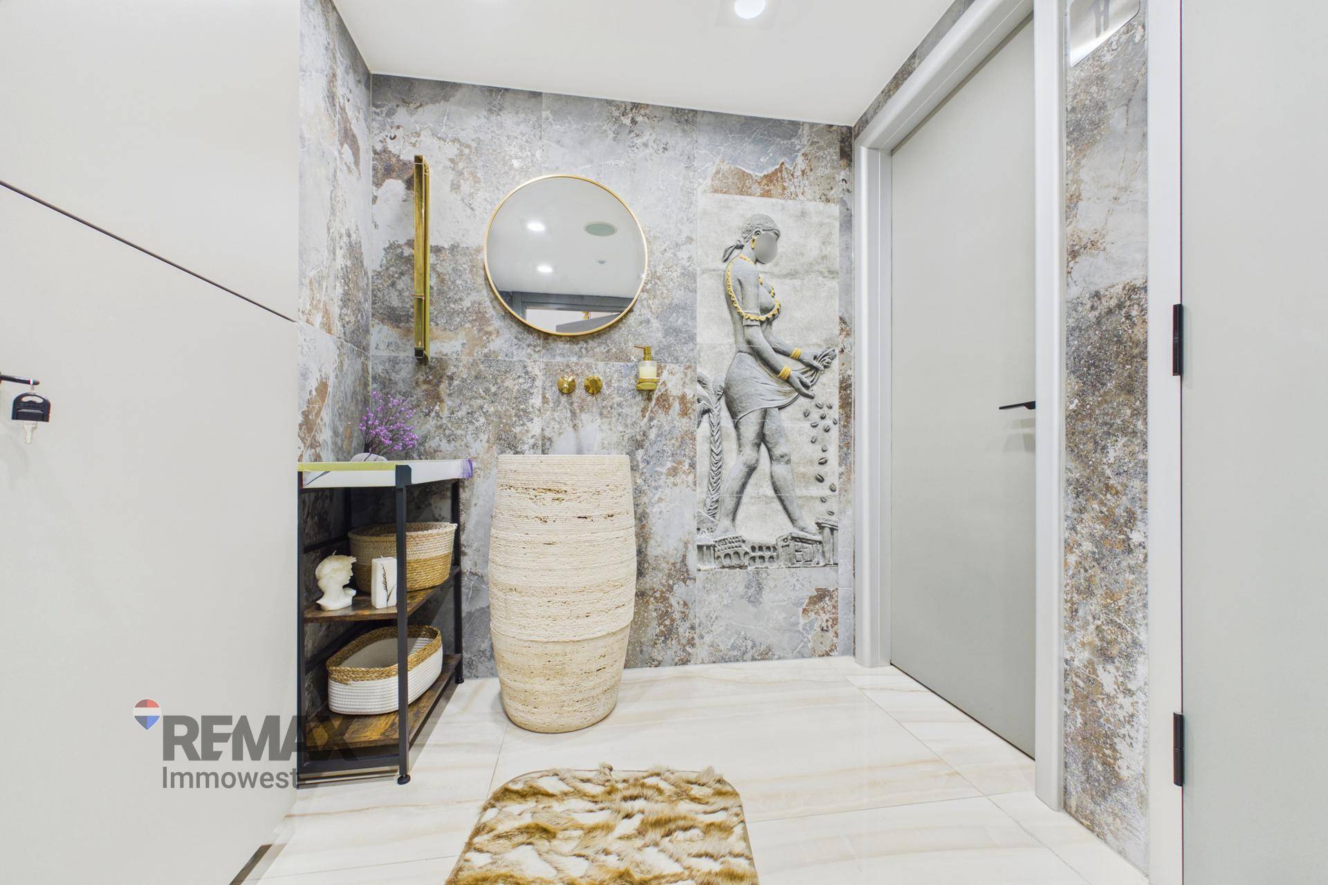 Modernes Badezimmer mit einzigartigem Waschbecken, runden Spiegel und dekorativen Wandfliesen in Erdtönen.