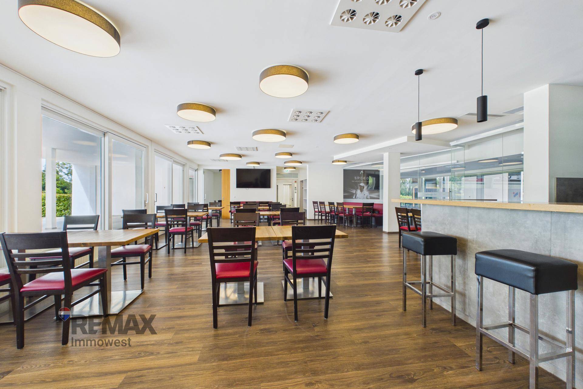 Moderner Restaurantbereich mit Barhockern, Holzboden und einem Flachbildschirm an der Wand.