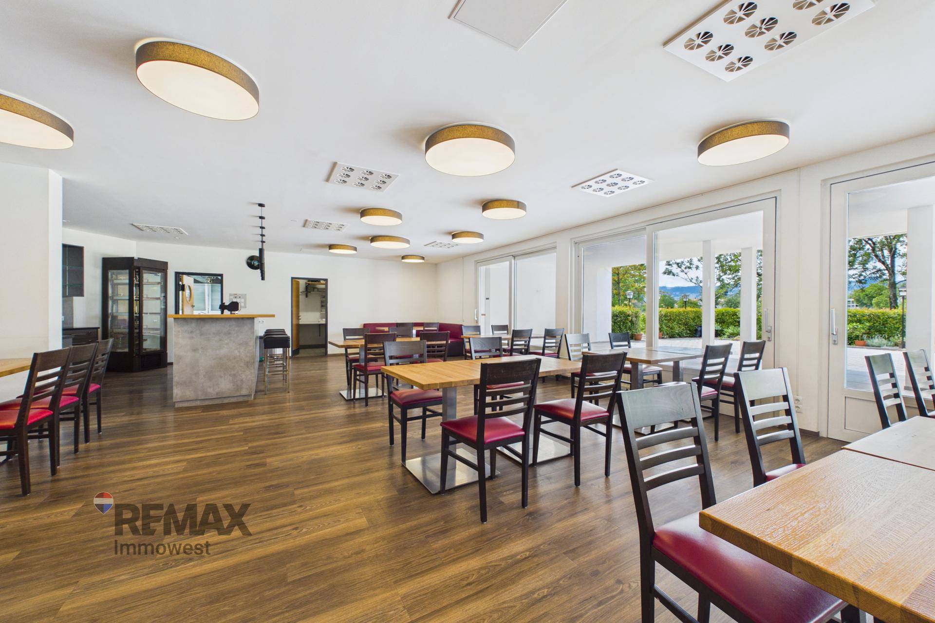 Heller Restaurantraum mit großen Fenstern, Holzboden und Blick ins Grüne.
