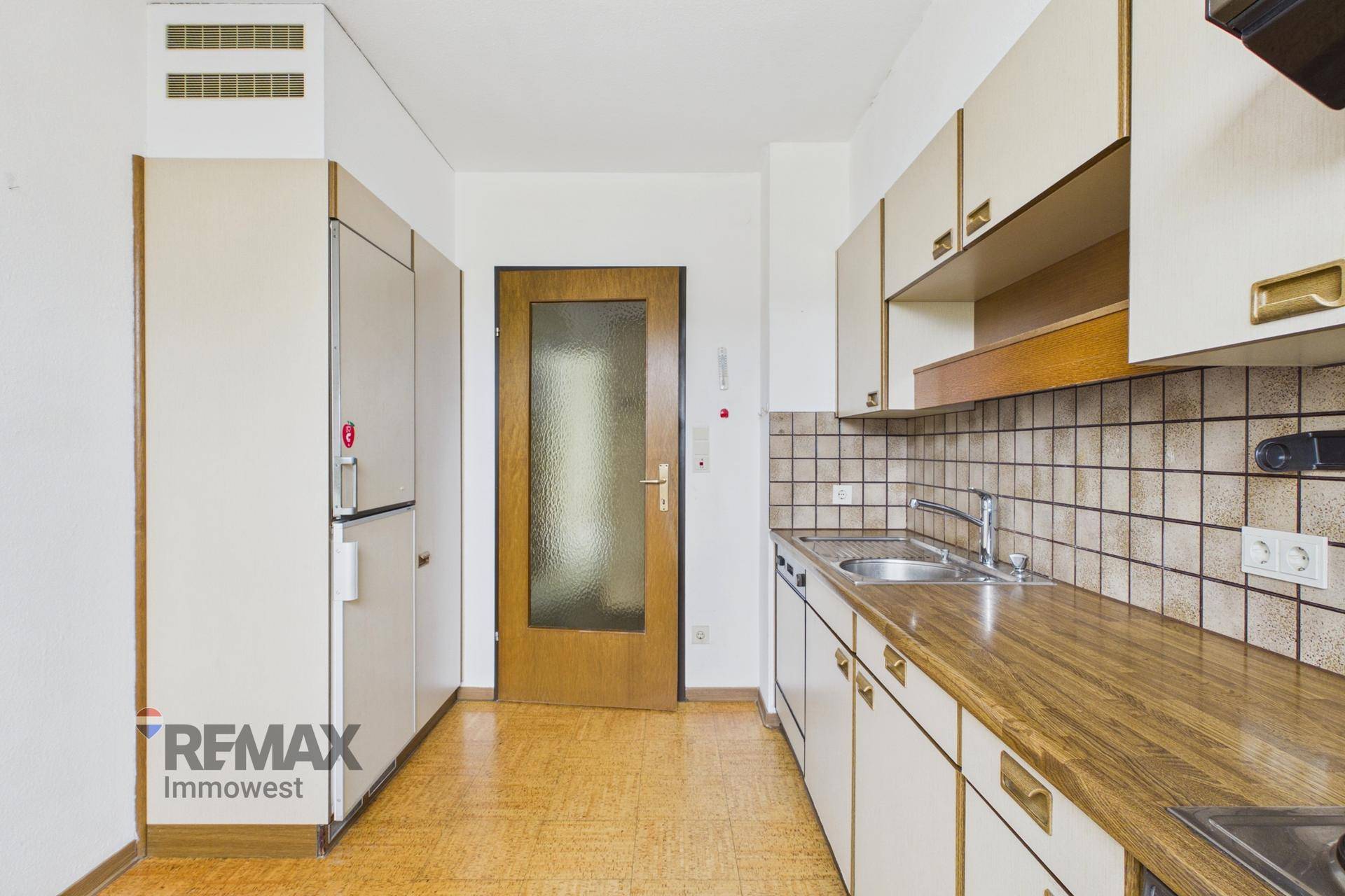 Küche mit älteren Einbaumöbeln, Kühlschrank und Zugang zu einem weiteren Raum.