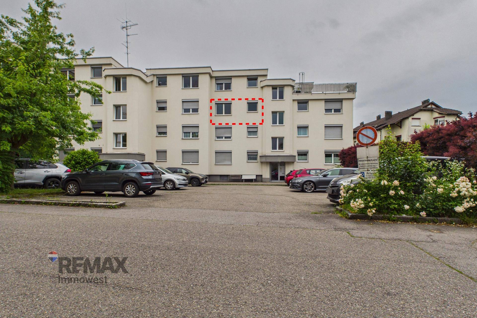Rückansicht des Mehrfamilienhauses mit Parkplätzen und begrüntem Umfeld.