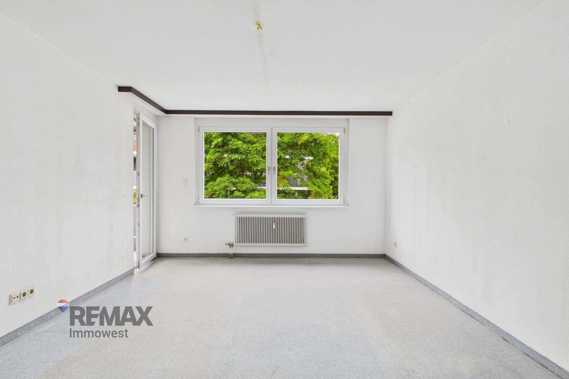 Geräumiges Wohnzimmer mit Teppichboden, großem Fenster und Zugang zum Balkon.