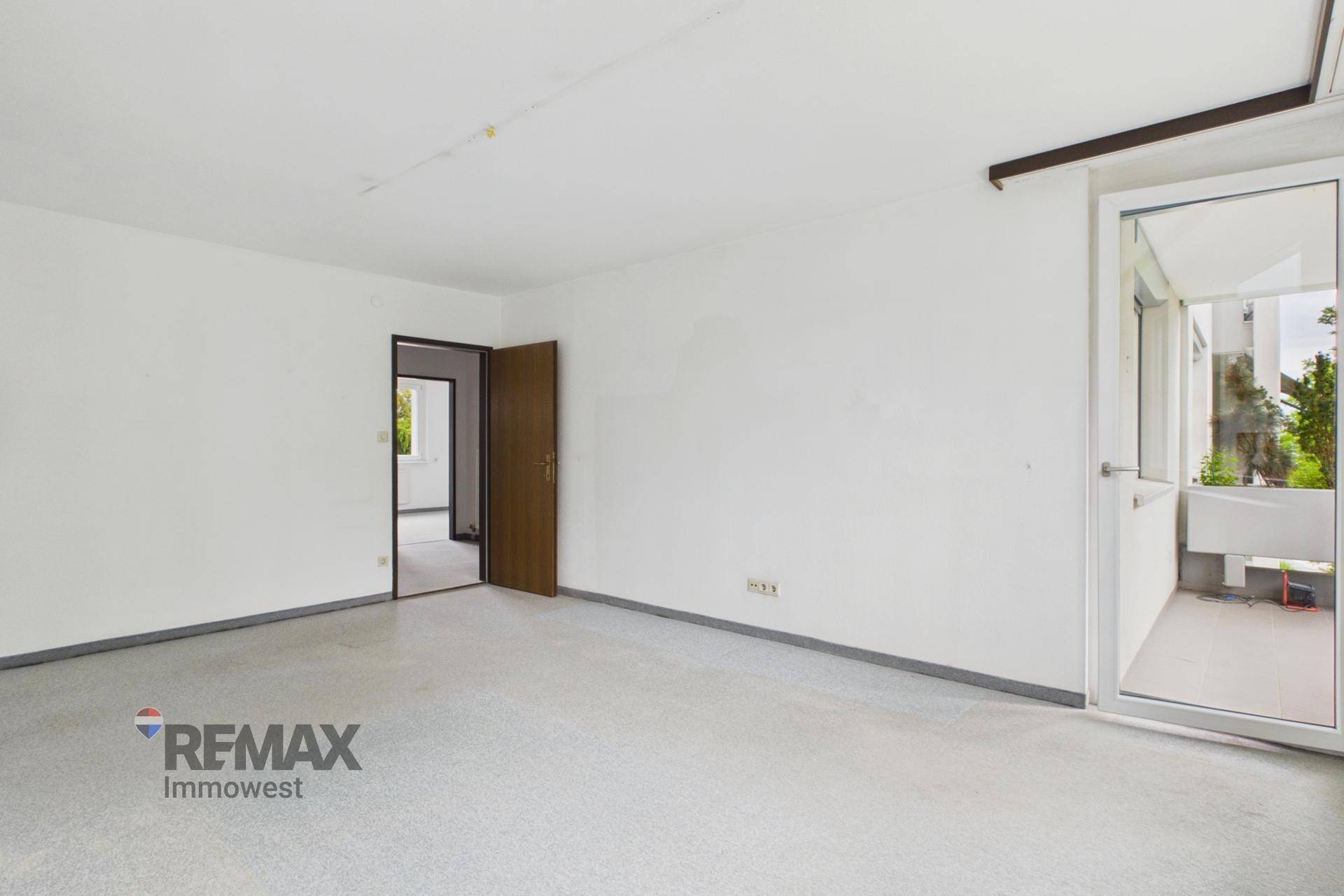 Helles Wohnzimmer mit Teppichboden und Zugang zum Flur sowie zum Balkon.