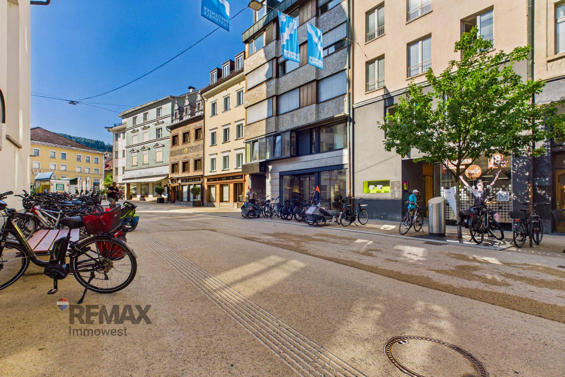 Belebtes Stadtbild mit Geschäften, Fahrrädern und historischen Gebäuden unter blauem Himmel.