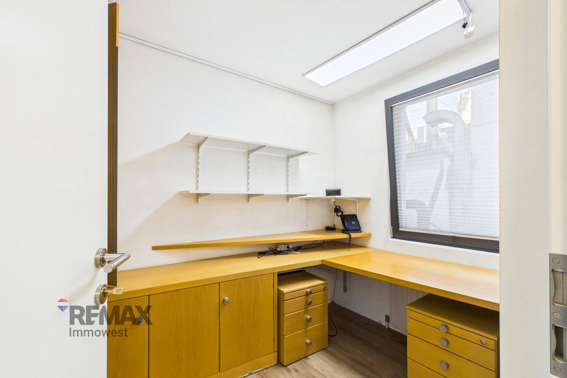 Kleines Büro mit Holzmöbeln, Schreibtisch, Regalen und einem Fenster.