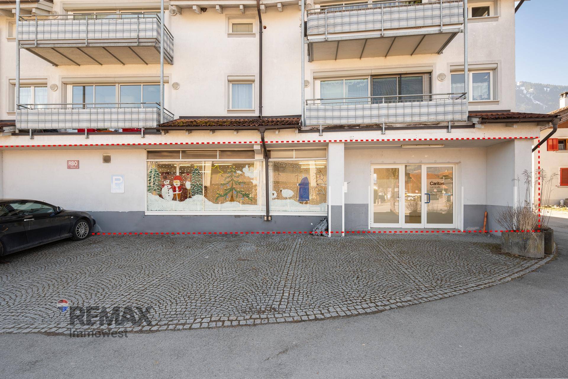Außenansicht des Gebäudes mit Geschäftsflächen im Erdgeschoss und Parkplätzen davor.