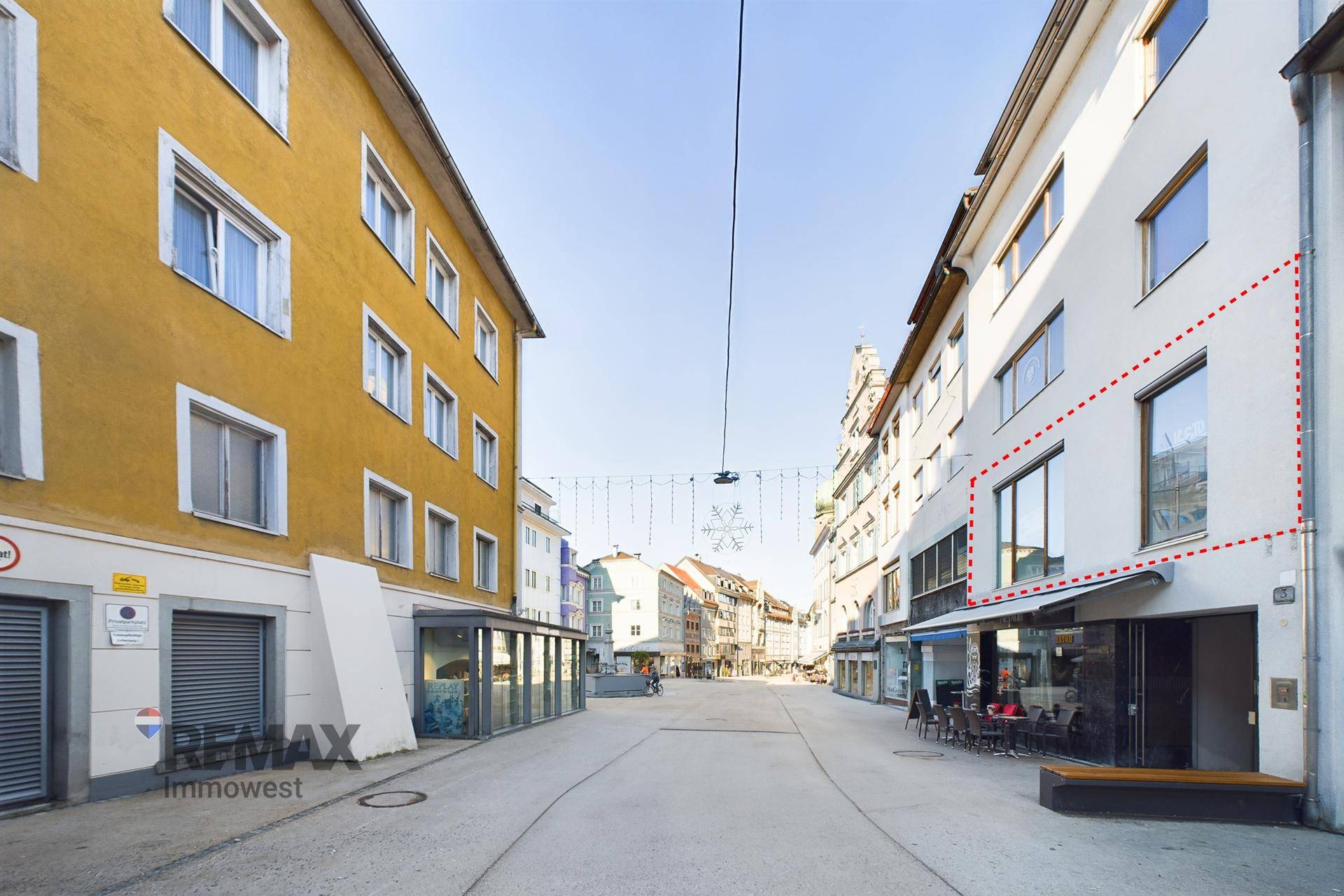 Weitwinkelansicht der Geschäftsfassade an einer städtischen Straße mit umliegenden Gebäuden und festlicher Dekoration.