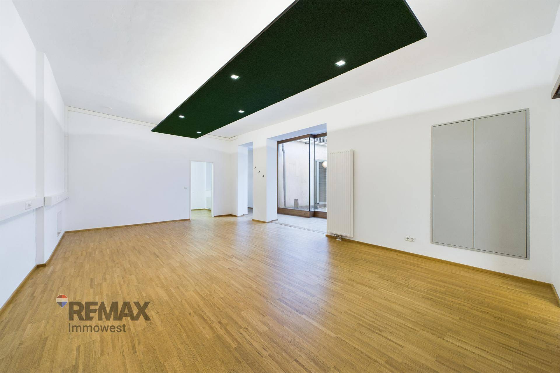 Geräumiger, leerer Büroraum mit Holzboden, weißen Wänden und einer dunklen, beleuchteten Deckenverkleidung.