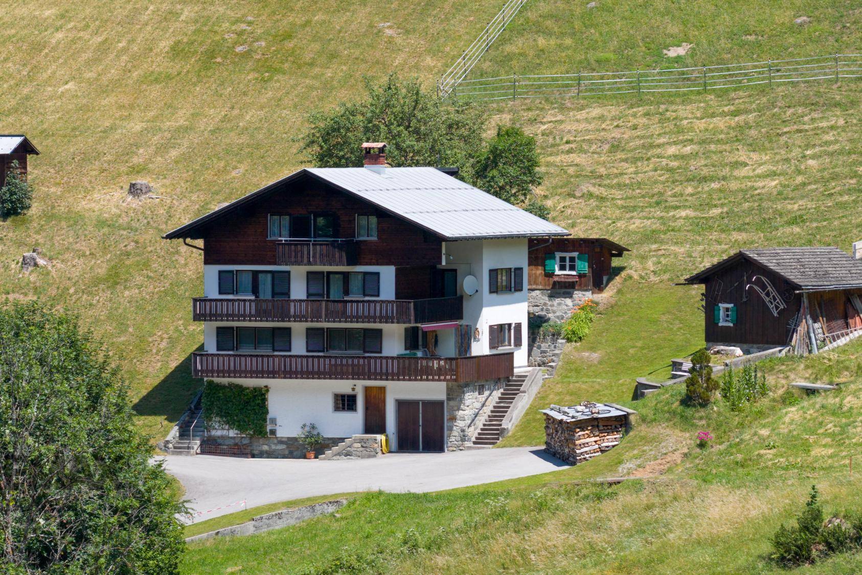 Alpines Wohnhaus mit Satteldach und Holzbalkonen, eingebettet in eine grüne Hügellandschaft.