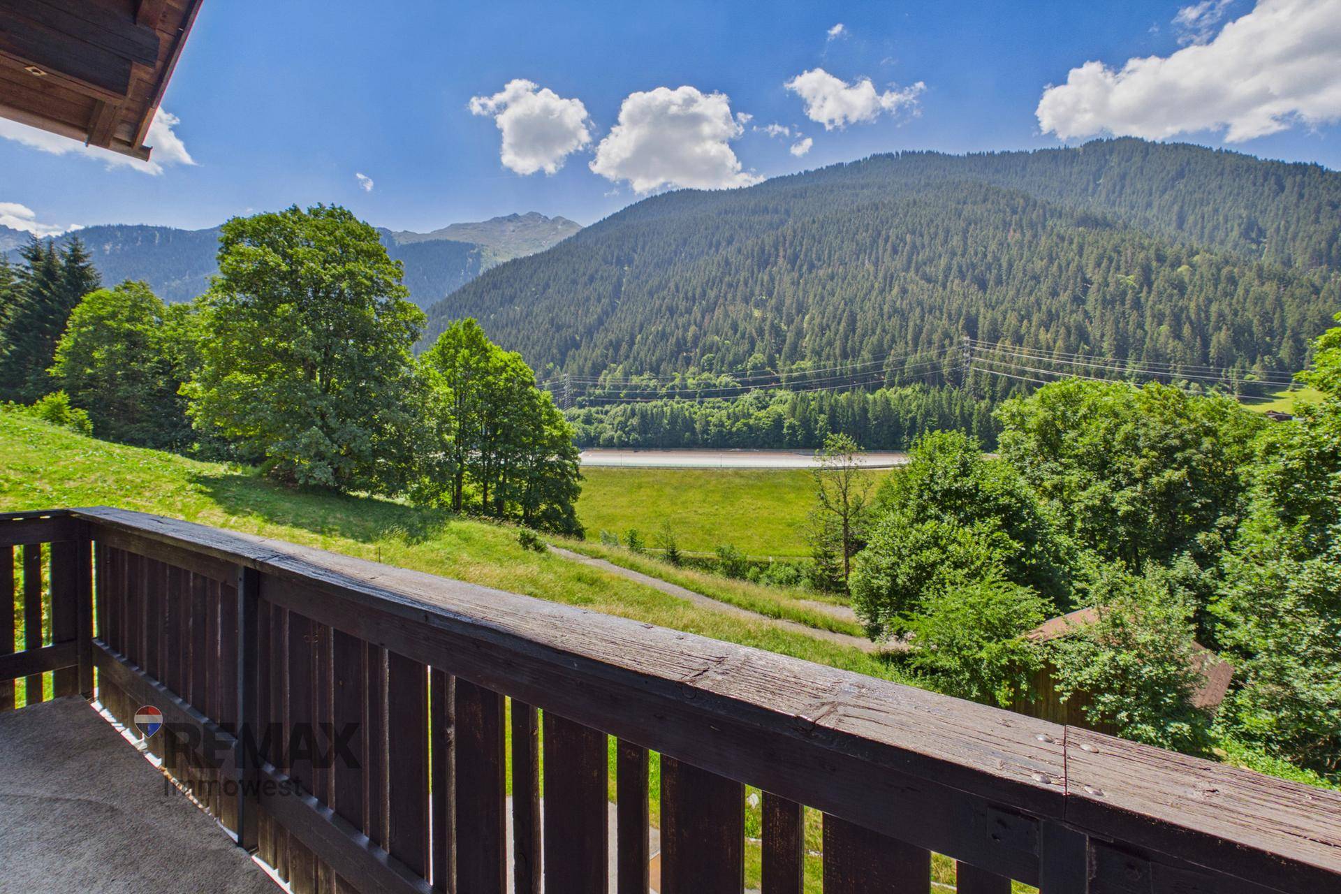 Malerischer Ausblick vom Balkon auf eine grüne Tallandschaft mit See und Bergen.