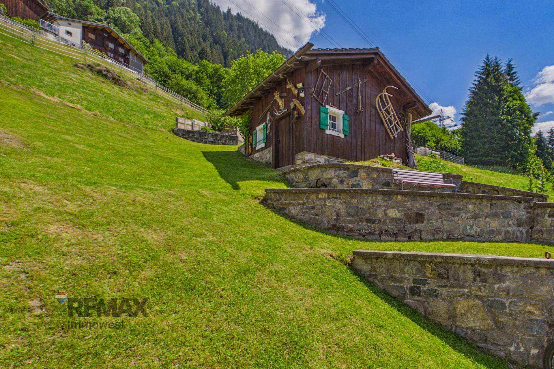 Rustikale Holzhütte mit traditioneller Dekoration auf einem grünen Hang mit Steinmauern.