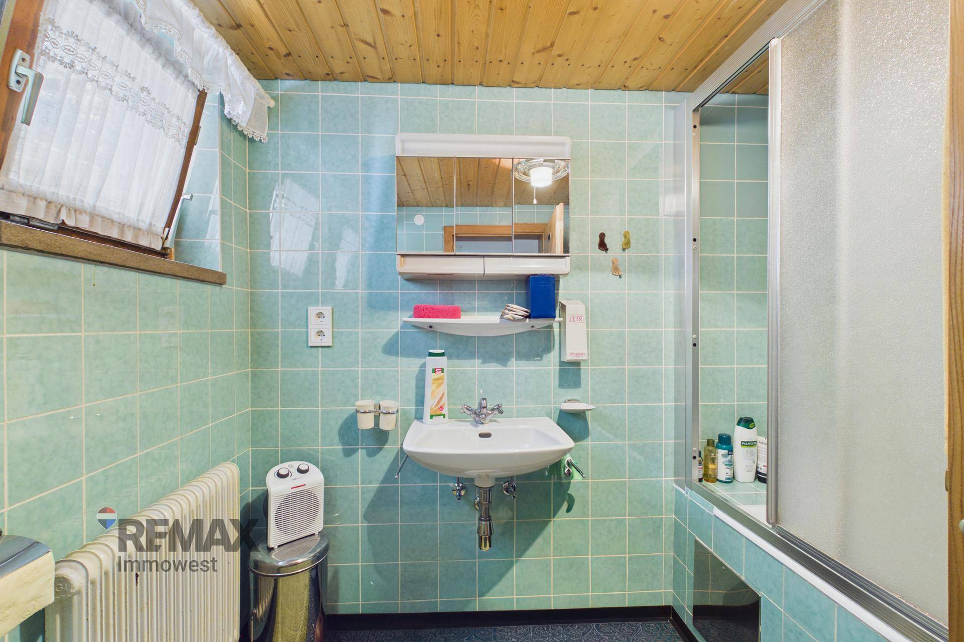 Traditionelles Badezimmer mit hellgrünen Fliesen, Waschbecken und Duschkabine.