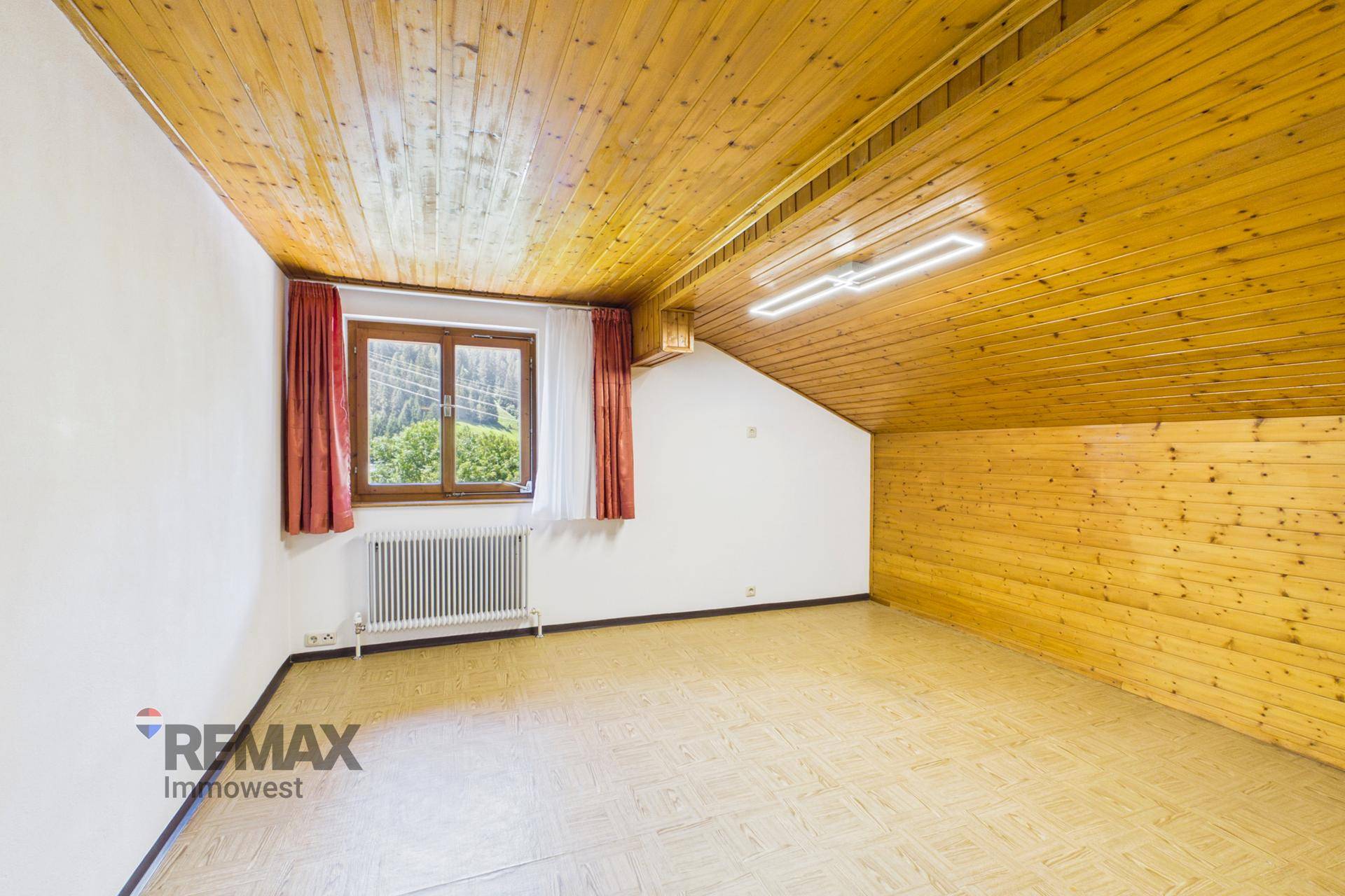 Helles Dachzimmer mit Holzdecke und Fensterblick ins Grüne, ausgestattet mit Heizkörper.