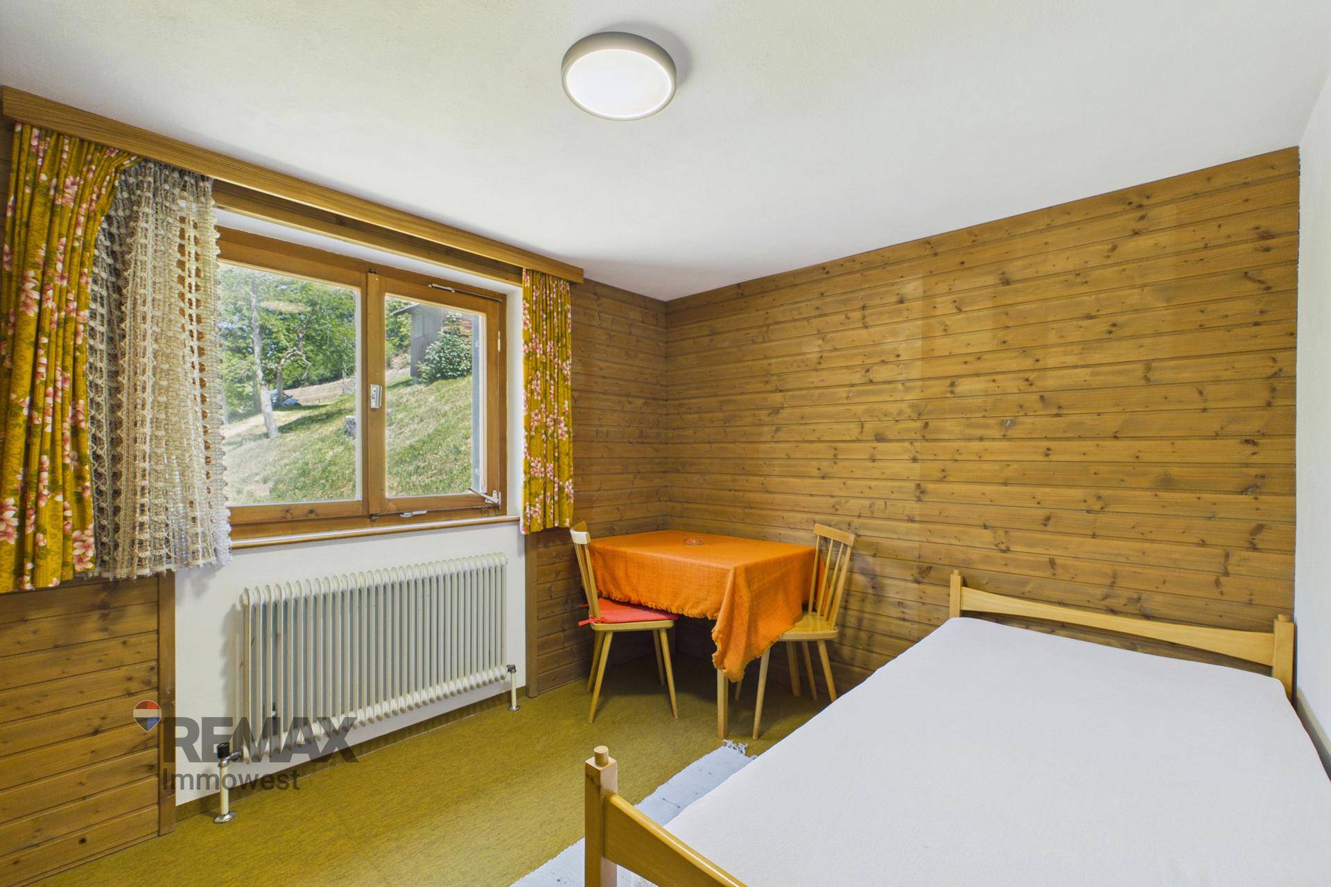 Gemütliches Schlafzimmer mit Holzvertäfelung, Einzelbett und kleinem Essbereich am Fenster.