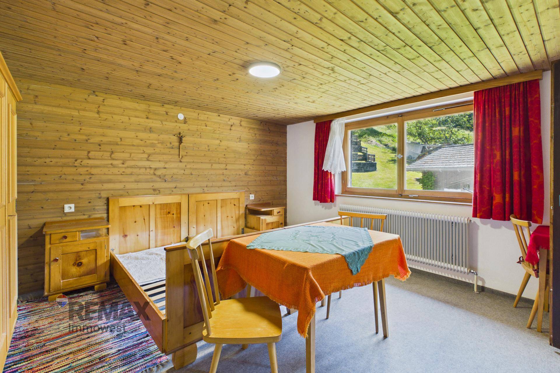Rustikales Schlafzimmer mit Holzvertäfelung, Doppelbett und Tisch, mit Blick ins Grüne.