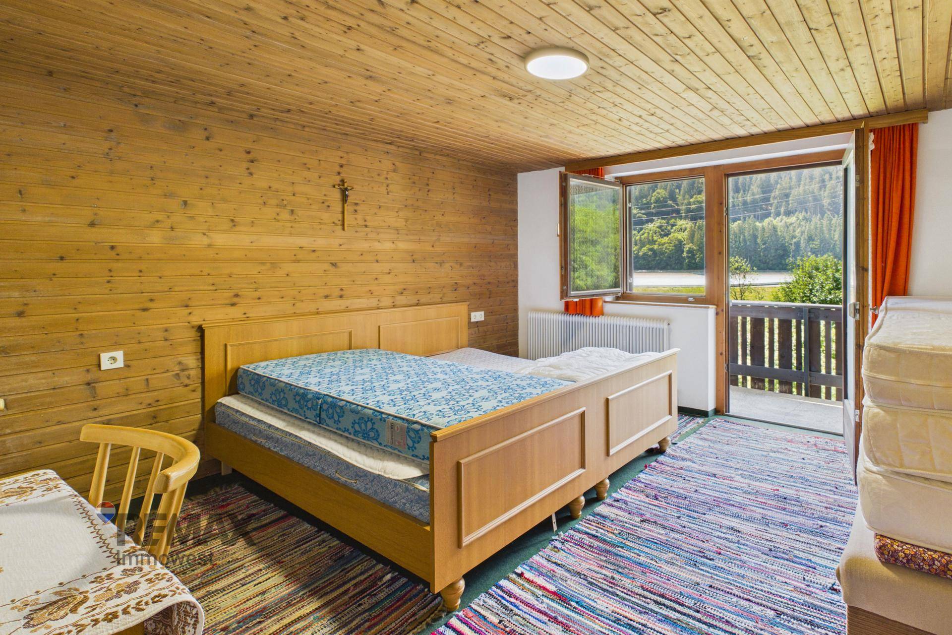 Schlafzimmer mit Holzvertäfelung, Doppelbett und Balkonzugang mit See- und Bergblick.