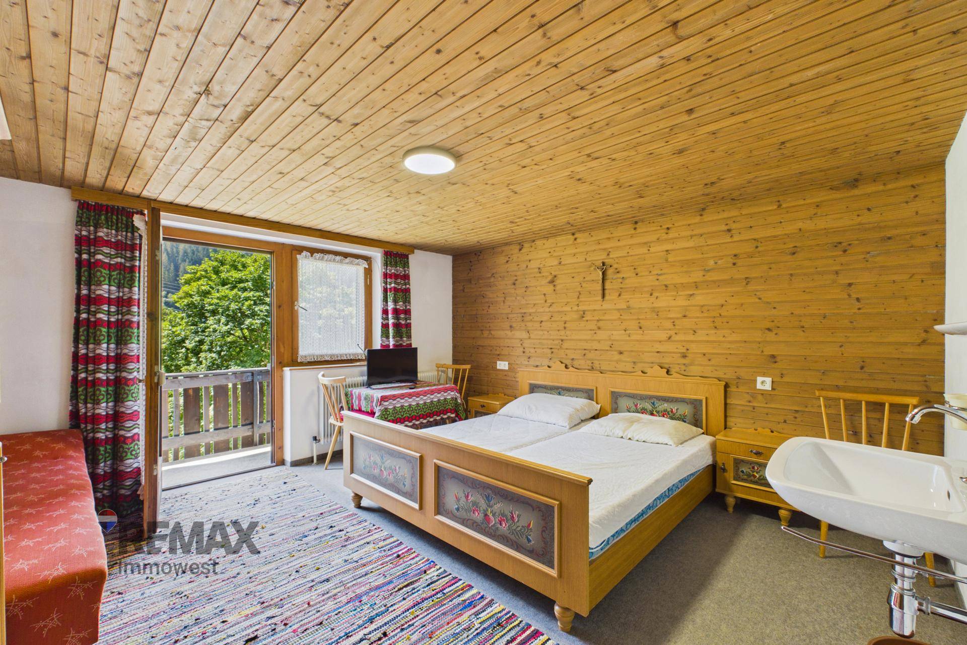 Schlafzimmer im Landhausstil mit Holzvertäfelung, Doppelbett, Waschbecken und Balkonzugang.
