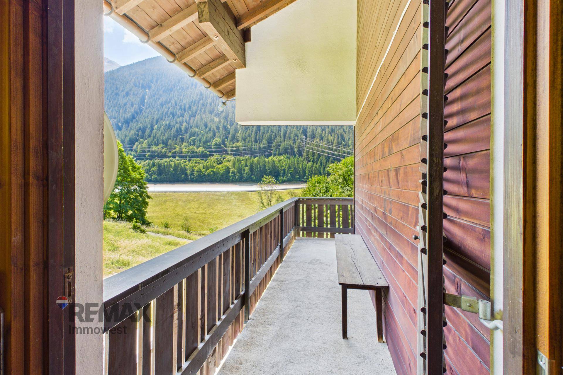 Langer Holzbalkon mit Sitzbank und weitem Blick über das Tal und die Berge.