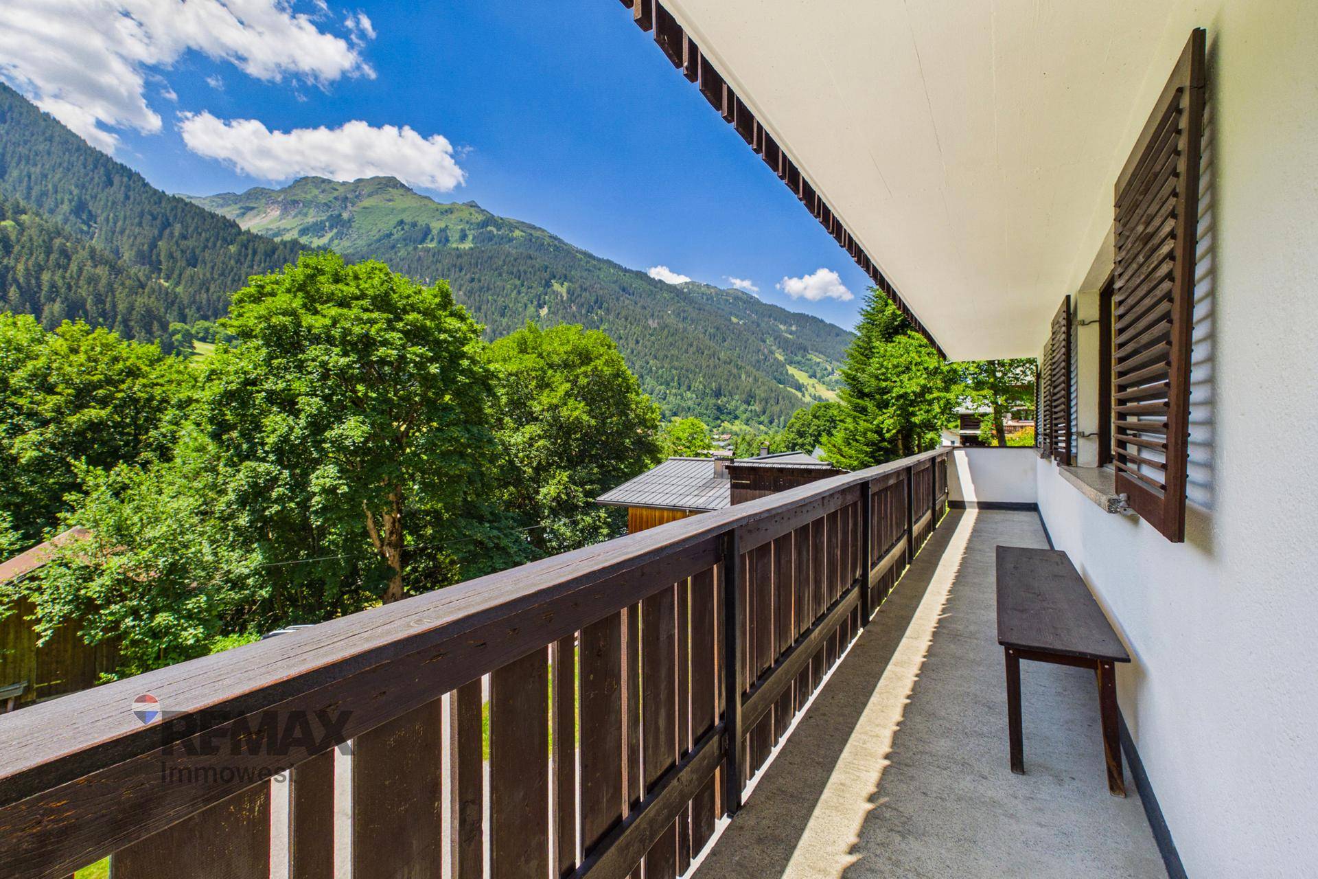 Langer Balkon mit Holzgeländer und Sitzbank, mit weitem Blick auf die Berglandschaft.