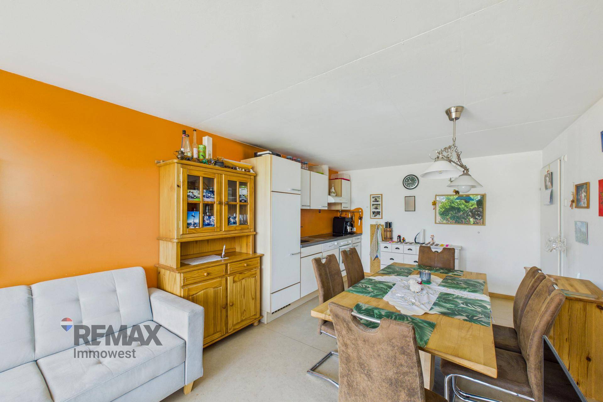 Offener Wohn- und Essbereich mit kleiner Küche, Esstisch und farbiger Akzentwand in Orange.