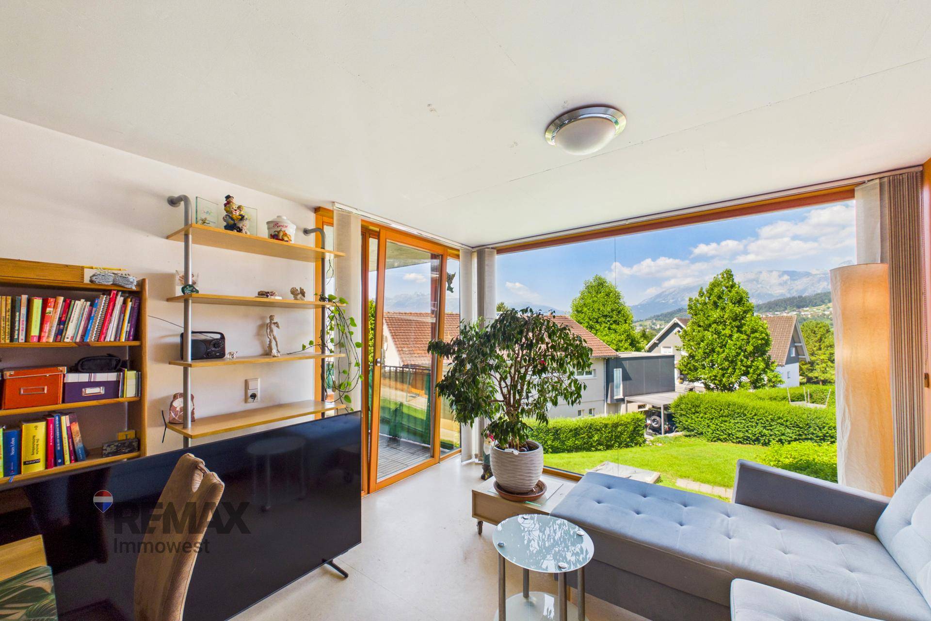 Gemütliches Wohnzimmer mit Sofa, Fernseher und weitem Blick auf die umliegende Landschaft und Berge.