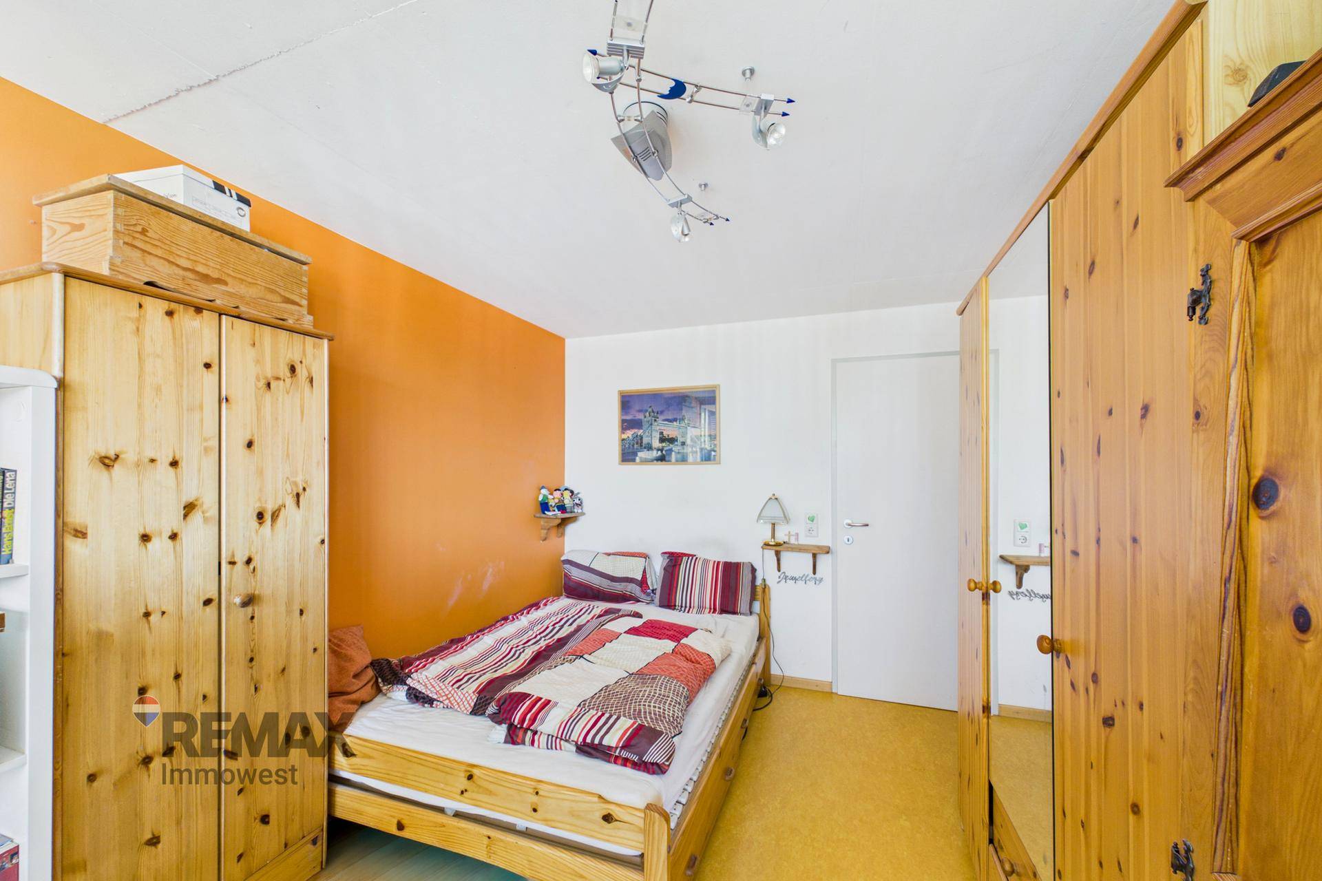 Gemütliches Schlafzimmer mit Holzmöbeln, orangefarbener Wand und karierter Bettdecke, einladend gestaltet.