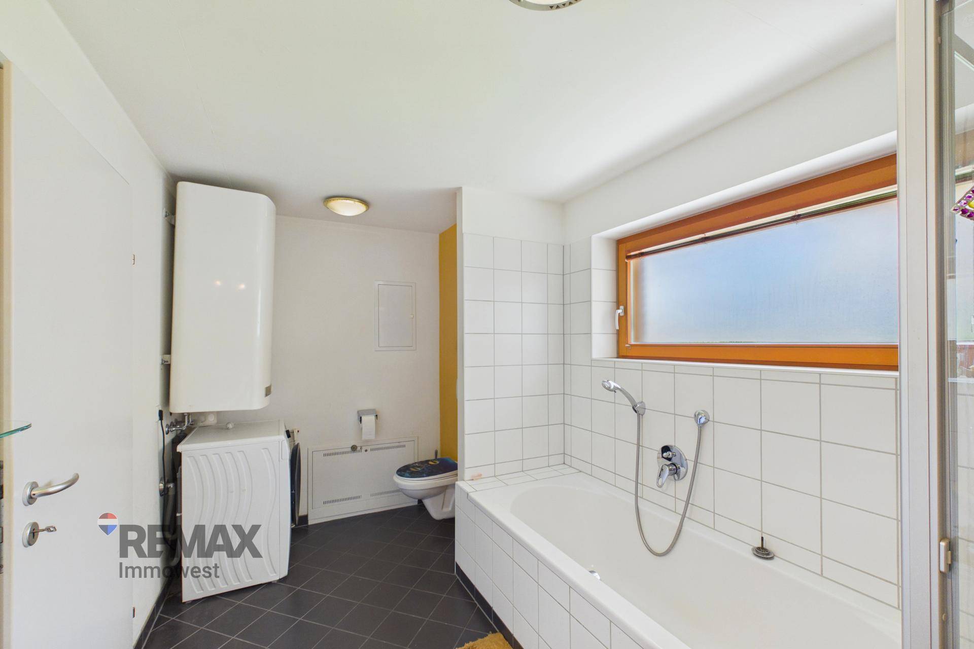 Funktionales Badezimmer mit Badewanne, Toilette und Waschmaschine, gut beleuchtet.