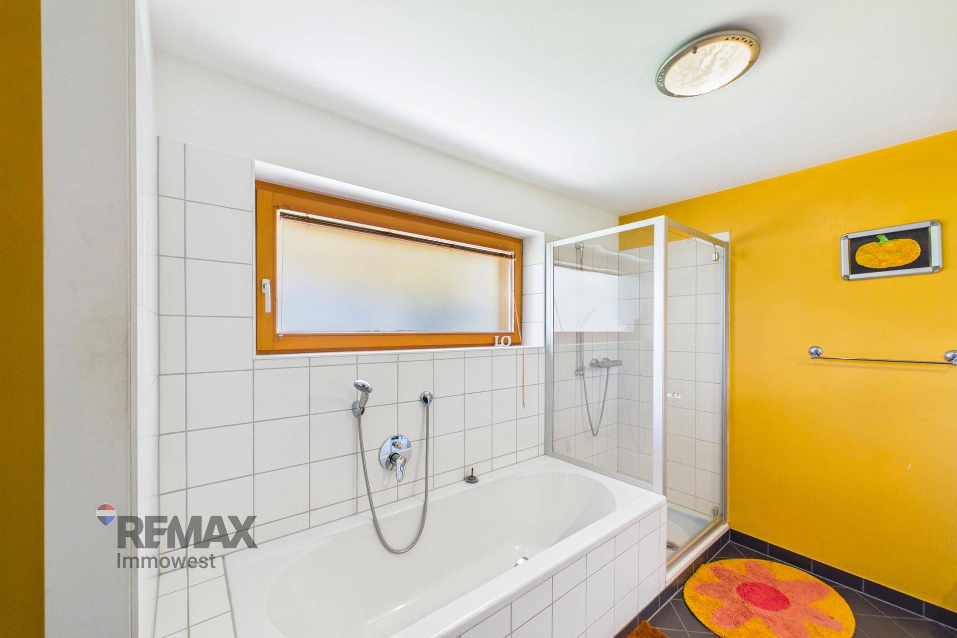 Badezimmer mit Badewanne, Duschkabine, weißen Fliesen und einem Fenster für Tageslicht.