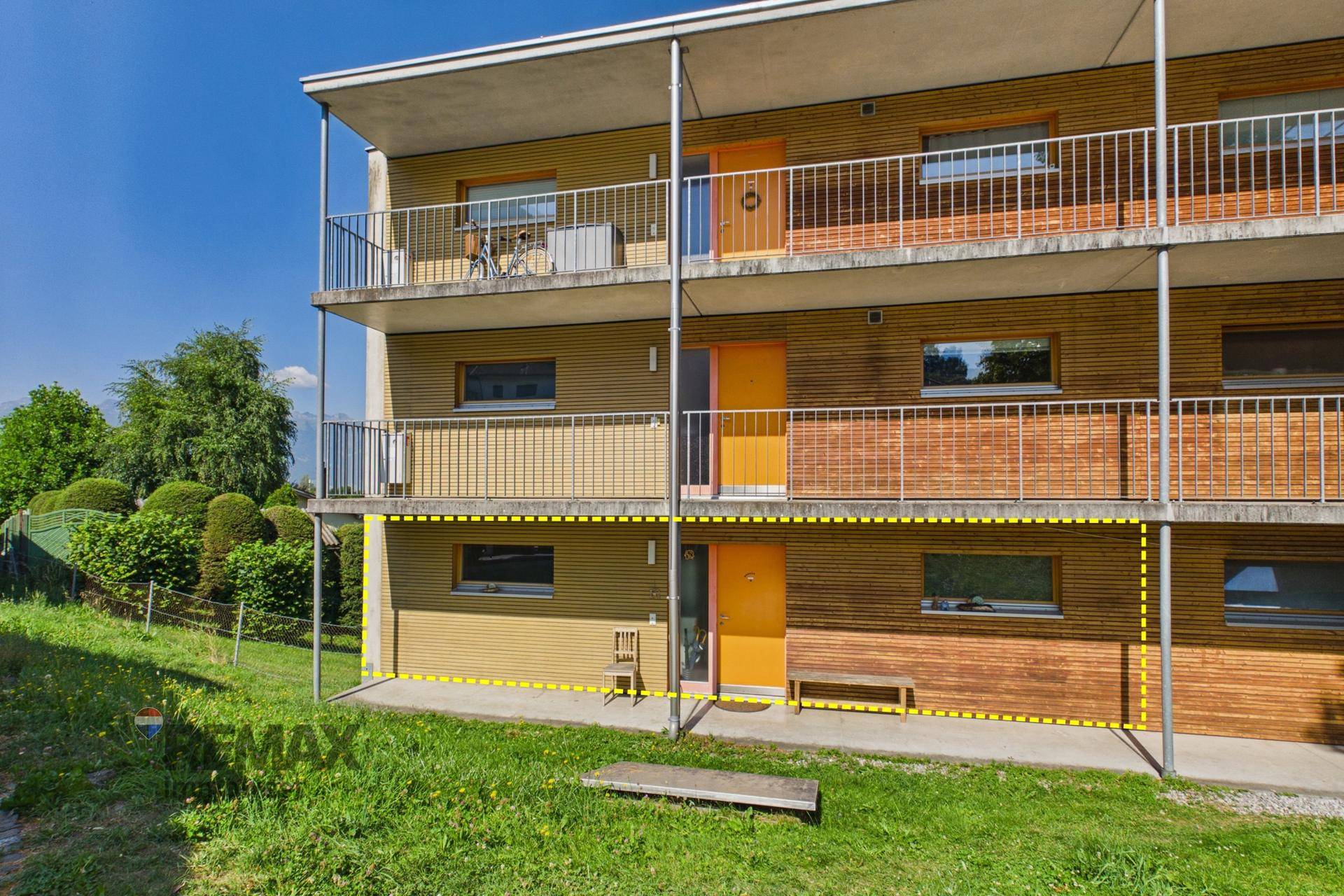 Mehrfamilienhaus mit mehreren Balkonen und Holzfassade, umgeben von Grünflächen und Natur.