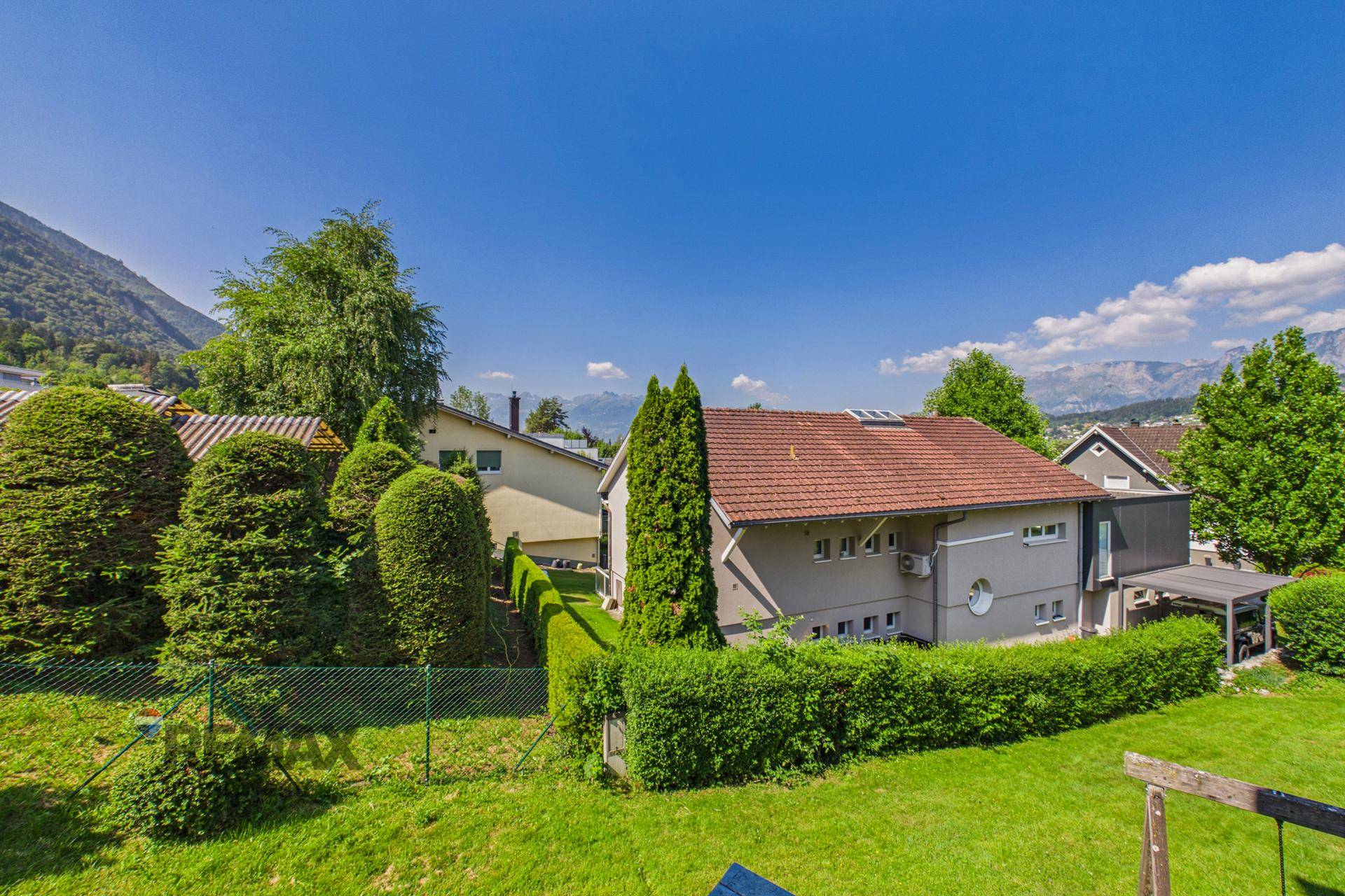 Außenansicht eines Hauses mit gepflegtem Garten, Hecken und beeindruckendem Bergpanorama im Hintergrund.