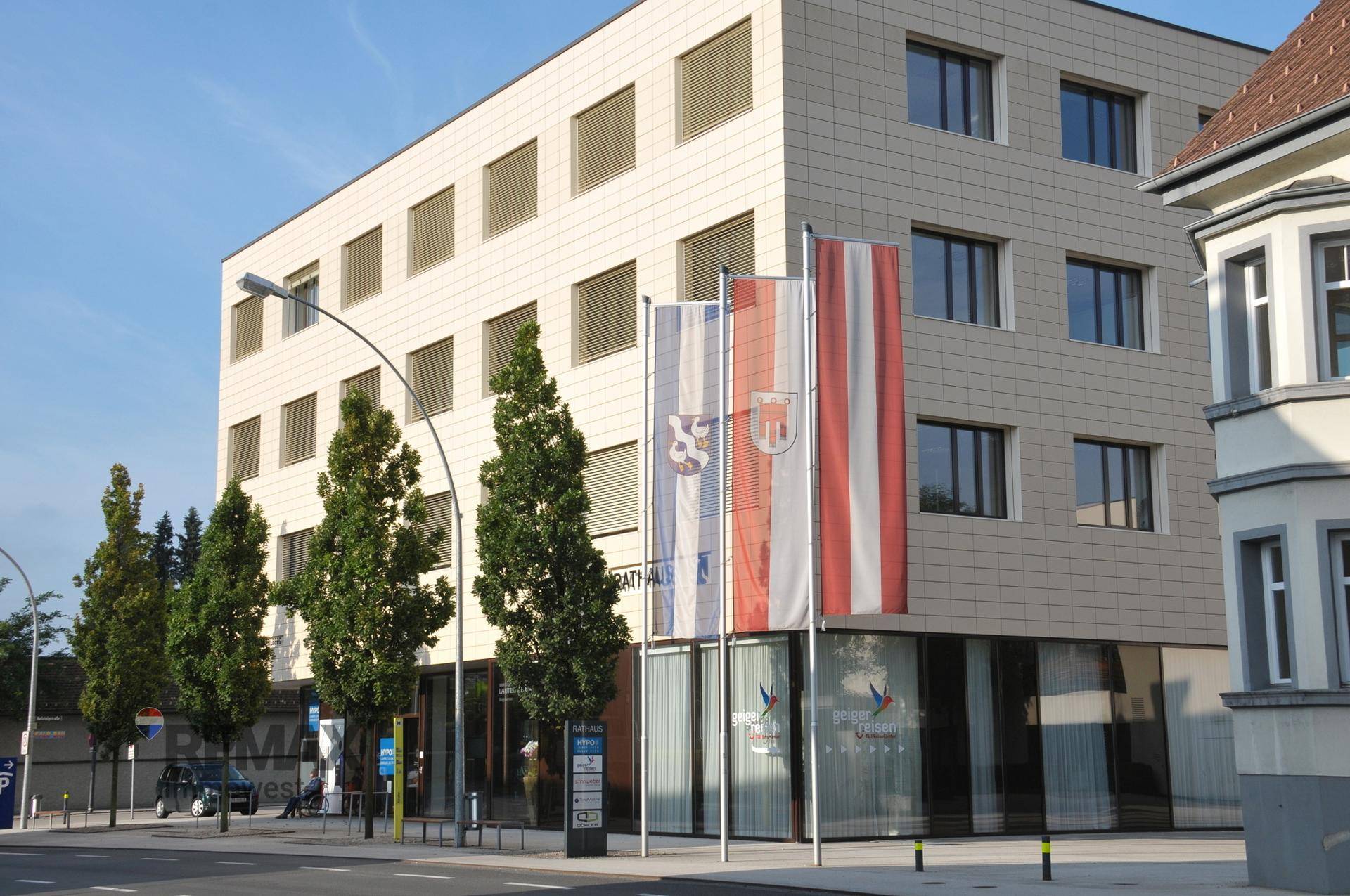 Moderne Gebäudefassade mit großen Fenstern und Fahnen davor, an einer städtischen Straße gelegen.
