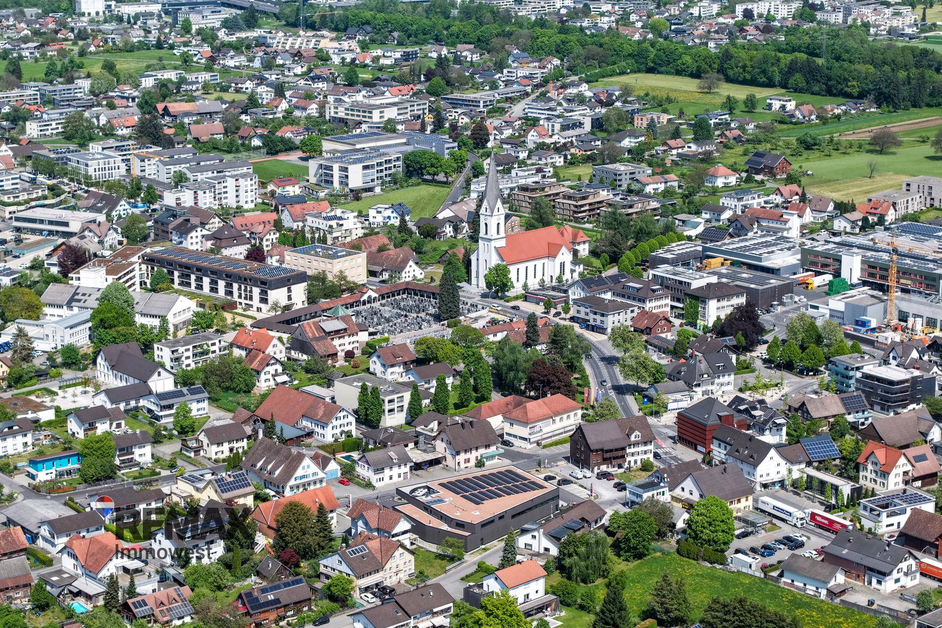 Luftaufnahme einer dicht besiedelten Stadt mit Wohngebieten, einer Kirche und viel Grün.