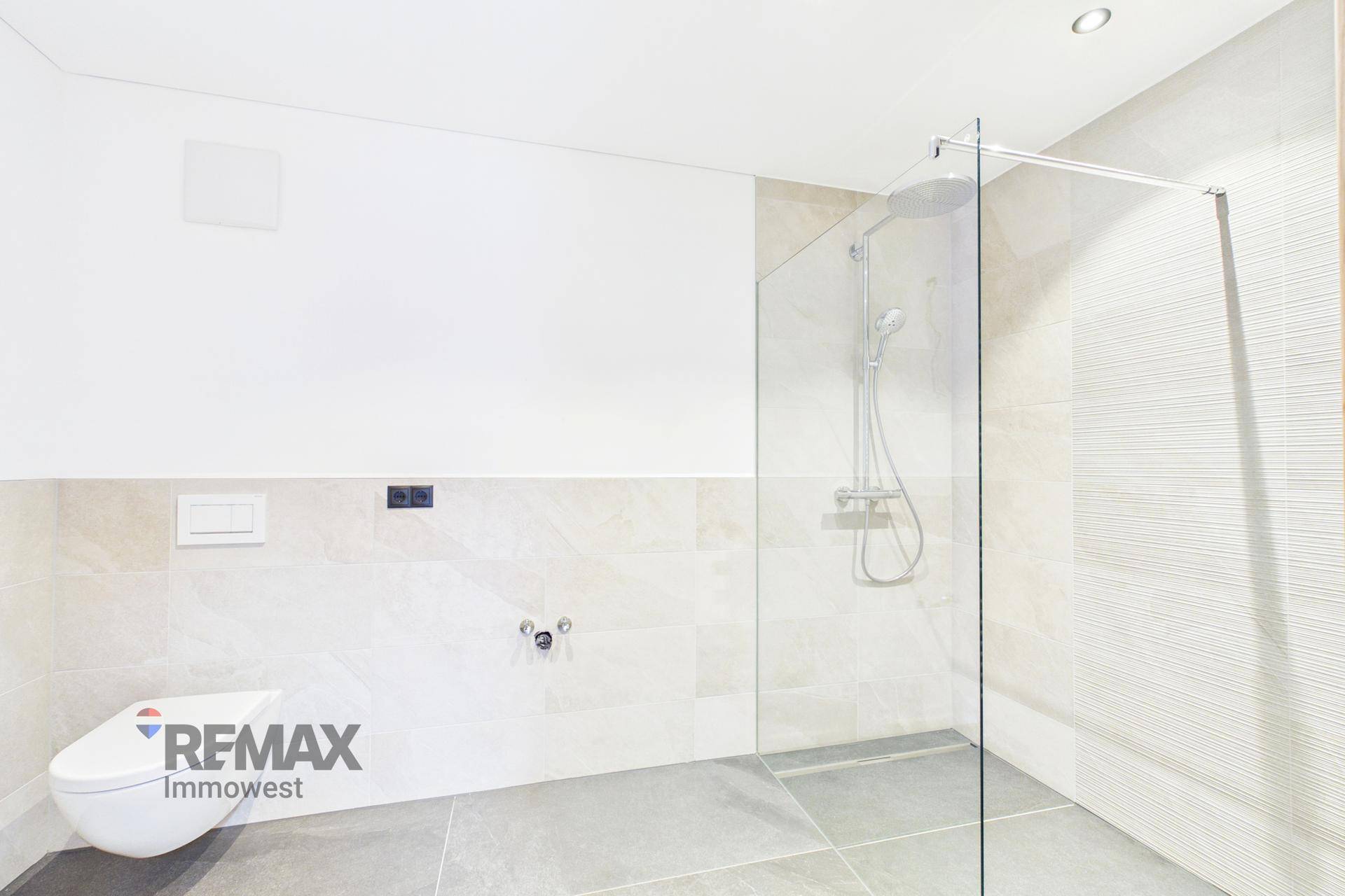 Modernes Badezimmer mit begehbarer Dusche, Wand-WC und hellen Fliesen.