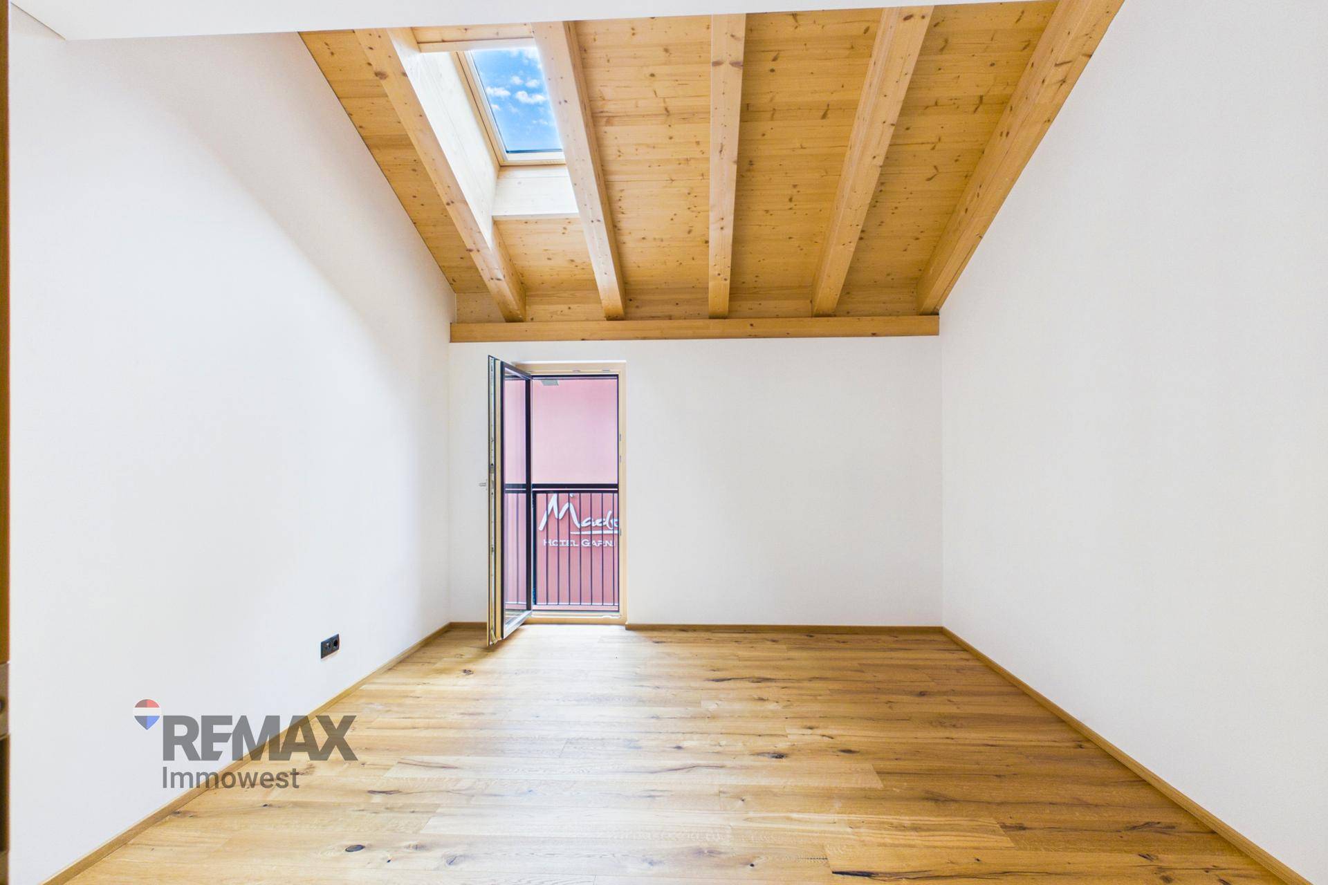 Helles Schlafzimmer mit Holzbalkendecke, Dachfenster und französischem Balkon.
