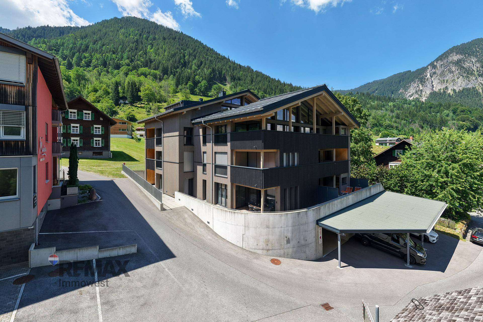 Neubau in den Bergen mit moderner Architektur, Carport und Blick auf die umliegende Natur.