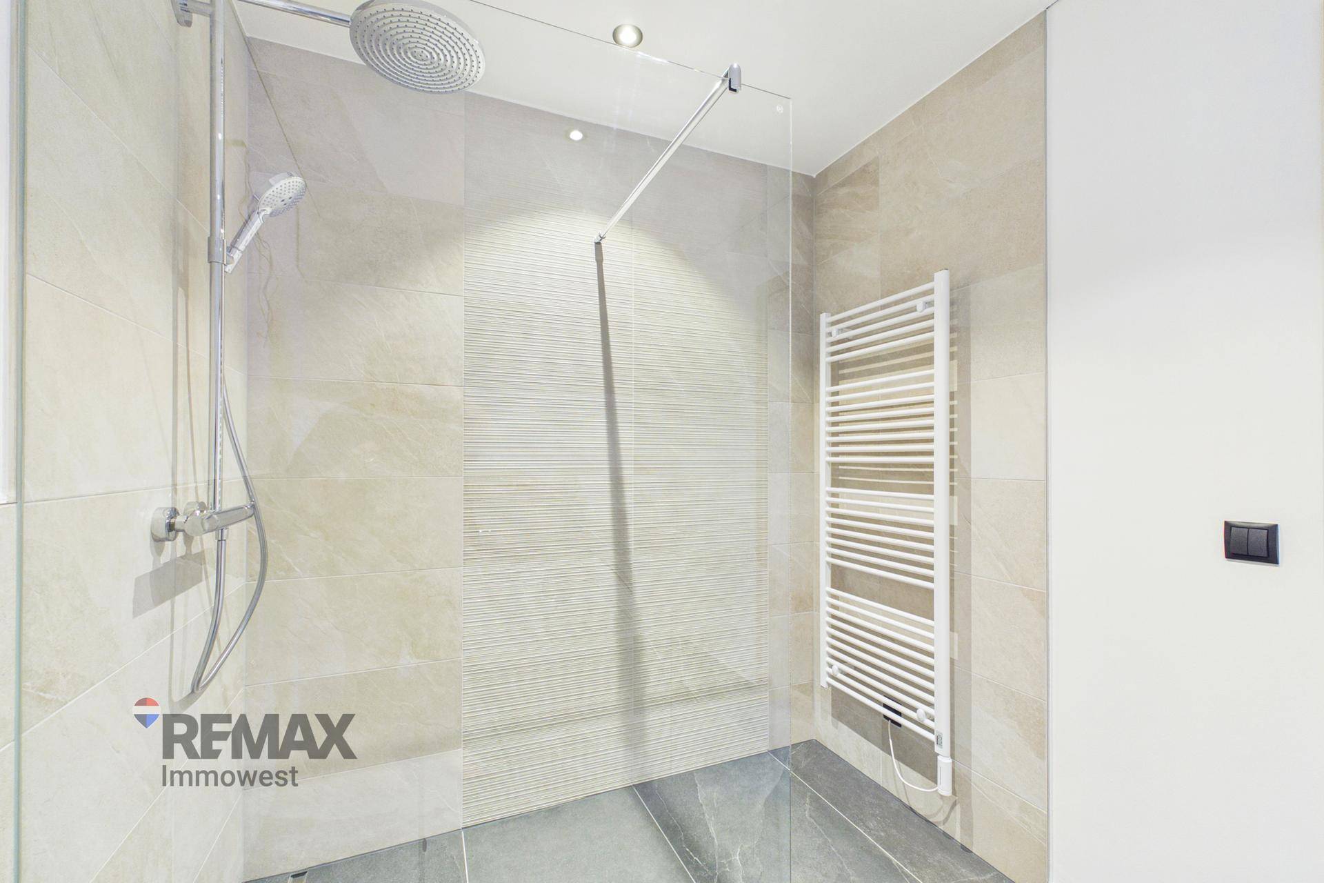 Elegantes Badezimmer mit Regendusche, Glasabtrennung und beheiztem Handtuchhalter.