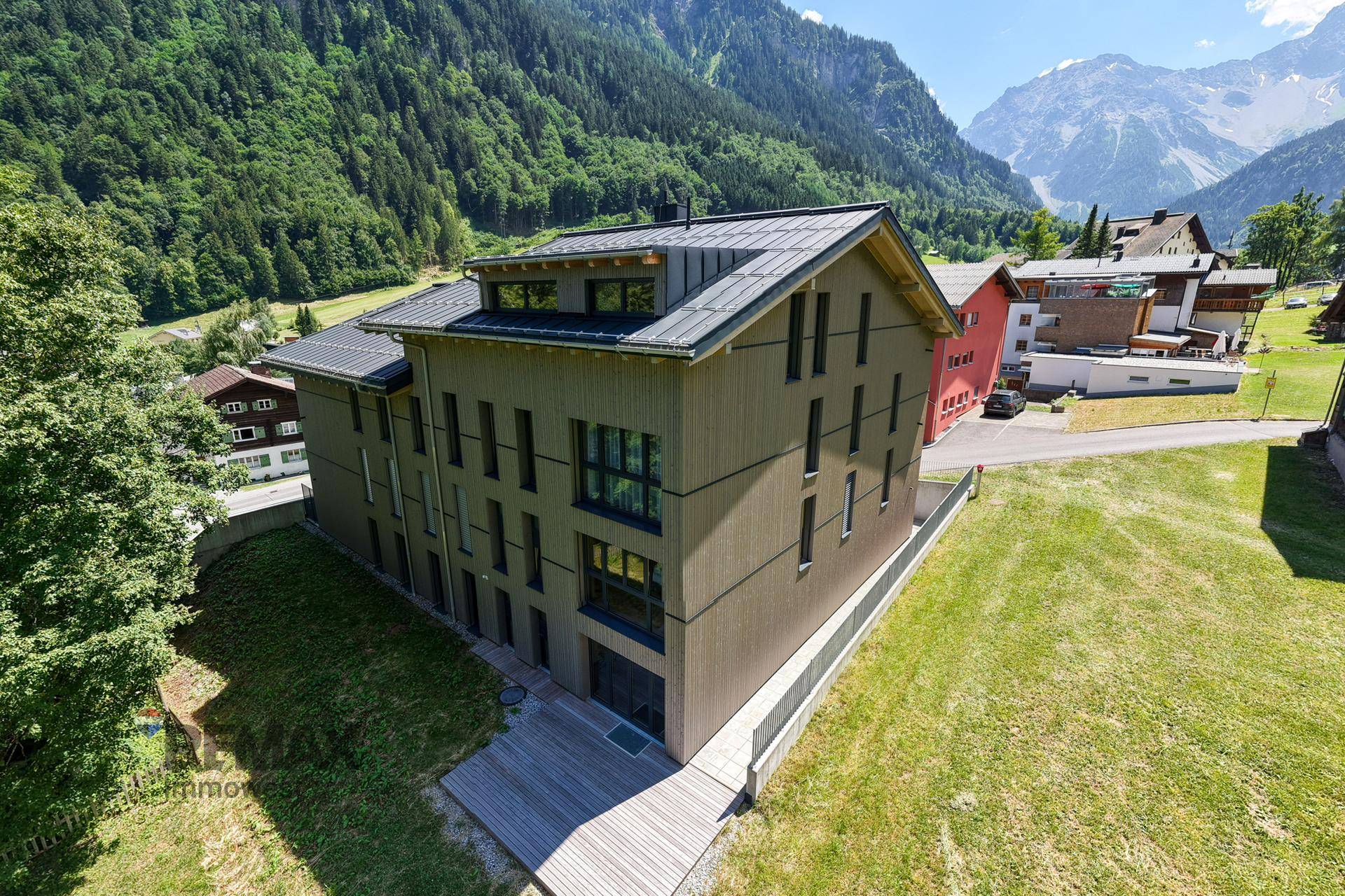 Zeitgenössisches Gebäude in alpiner Landschaft mit Holzfassade und weiten Grünflächen.
