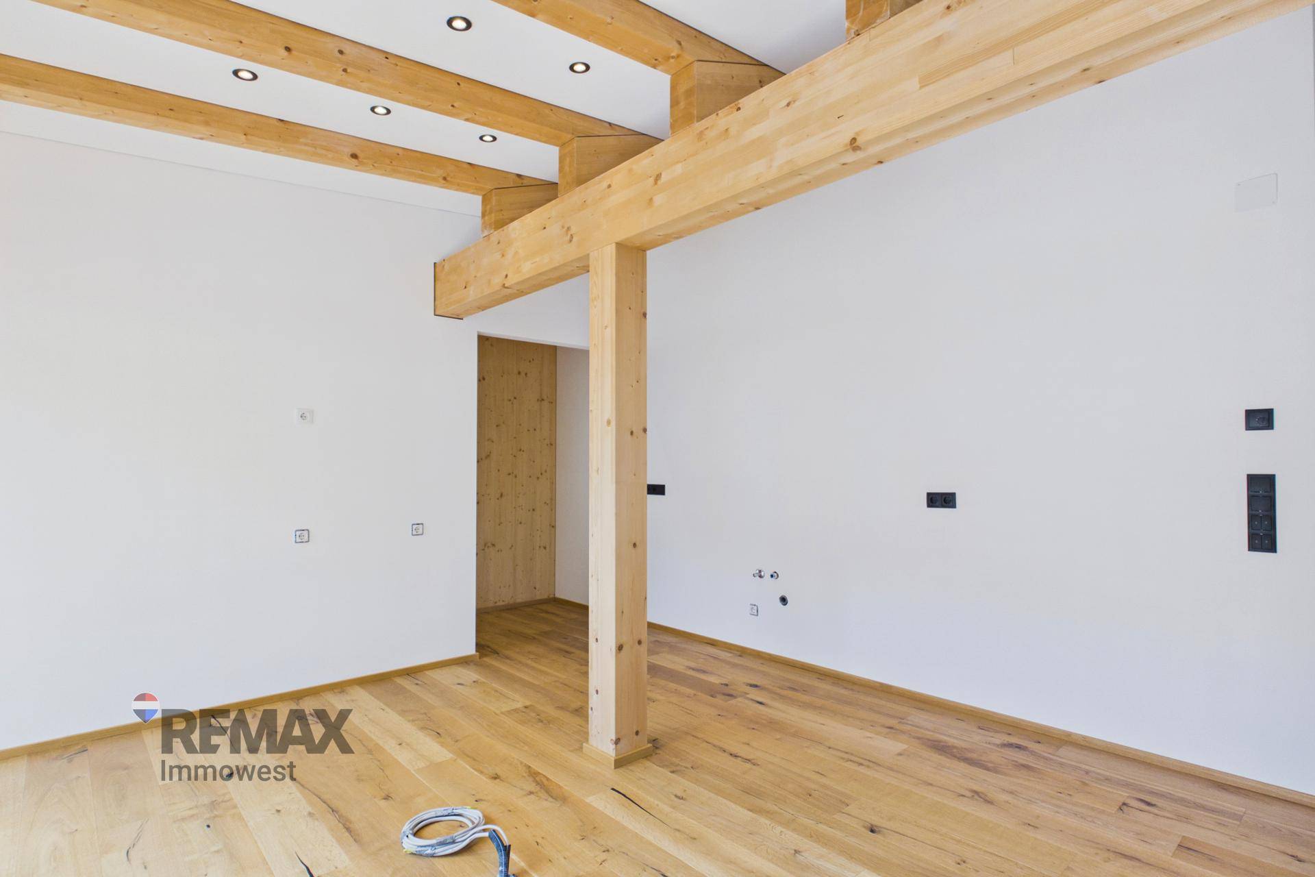 Geräumiger Wohnbereich mit Holzbalken und vorbereiteten Anschlüssen für die Einrichtung.
