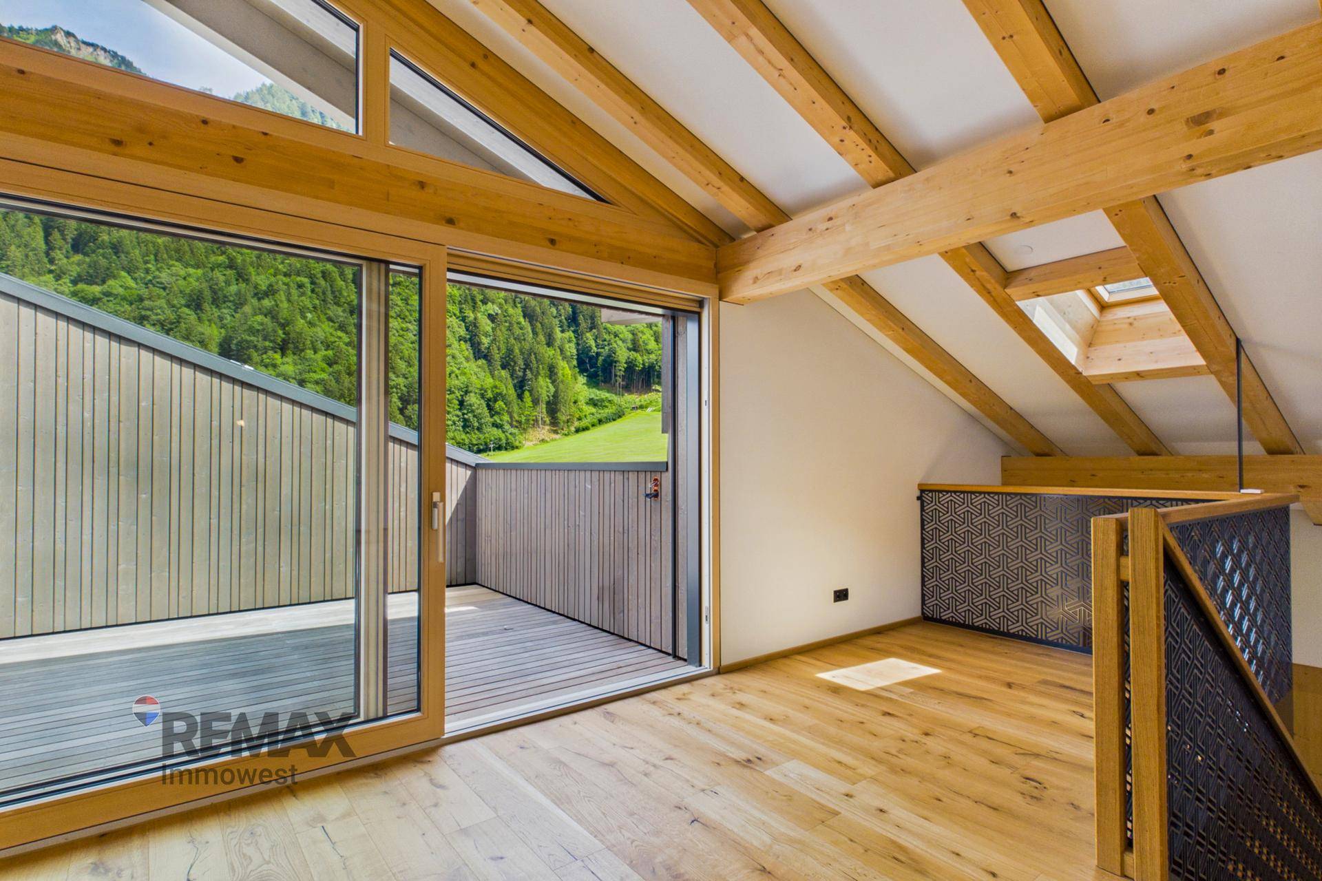 Heller Wohnraum mit Holzbalken, Dachfenster und direktem Zugang zur Außenterrasse.